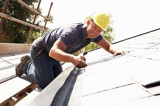 Construction worker installing roof shingles with measuring tool on sloped roof.