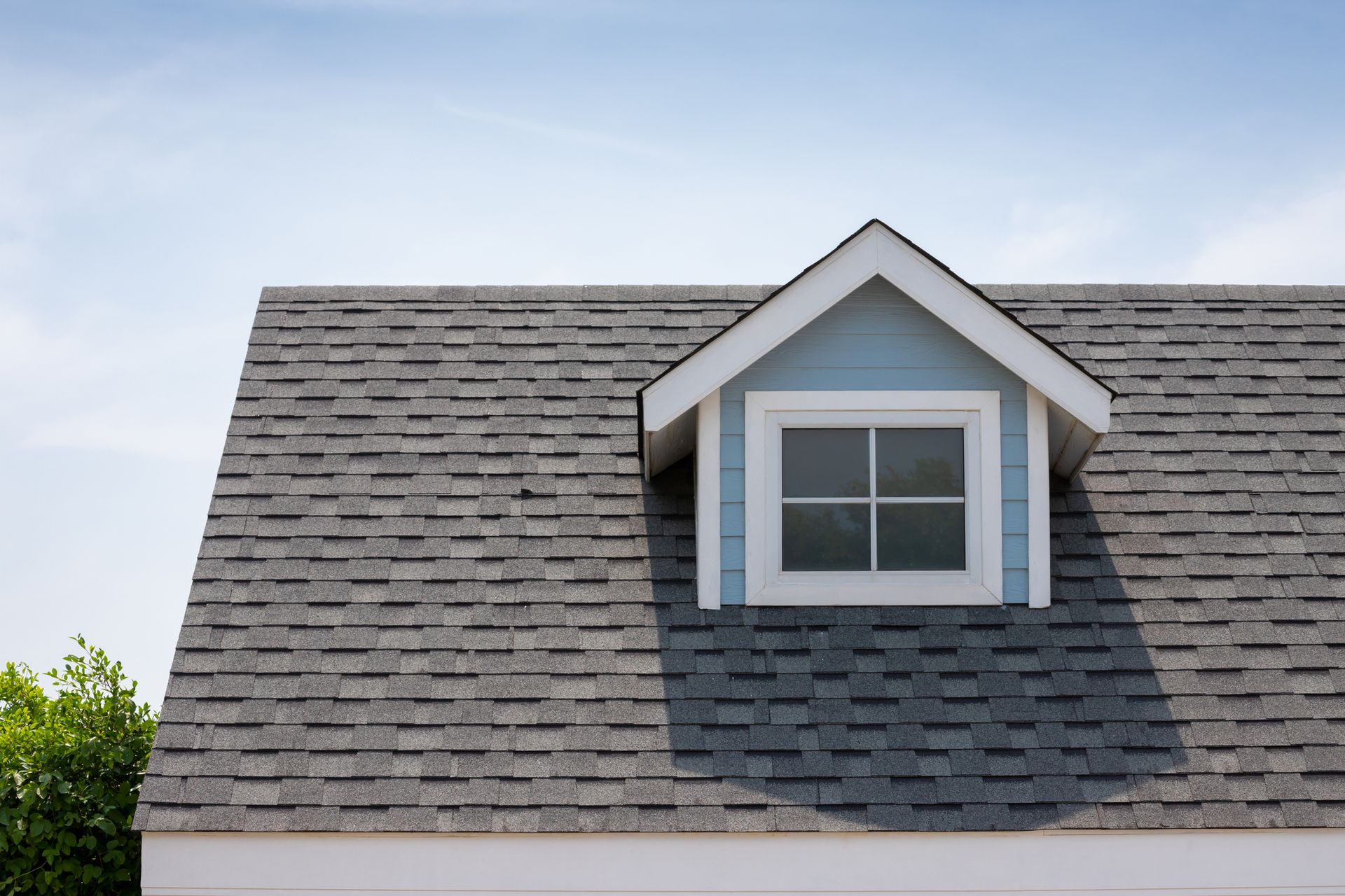 Dormer window on a gray shingled roof against a bright blue sky.