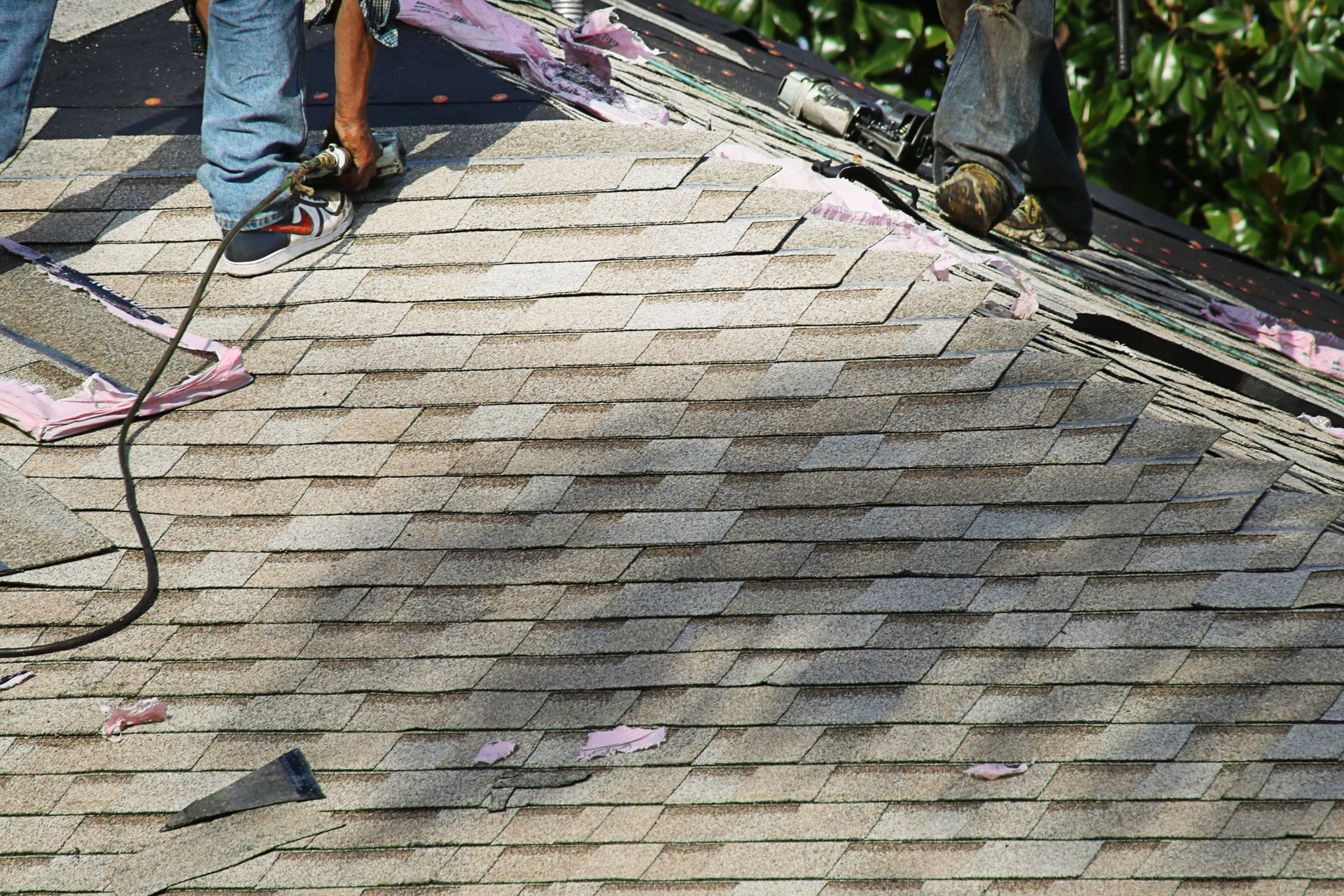 Workers removing old asphalt roof shingles.