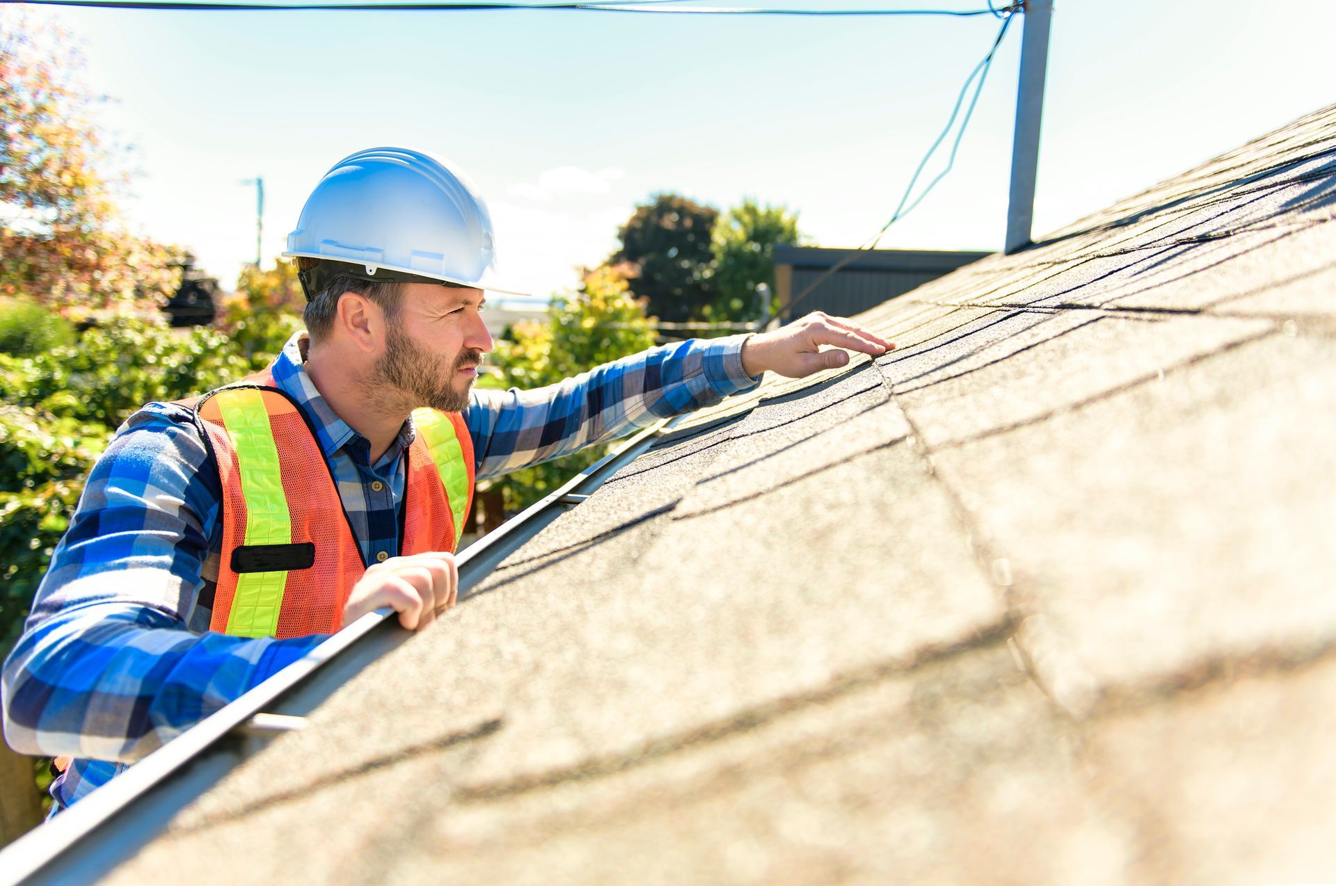 Man in hard hat and vest inspecting a shingle roof.