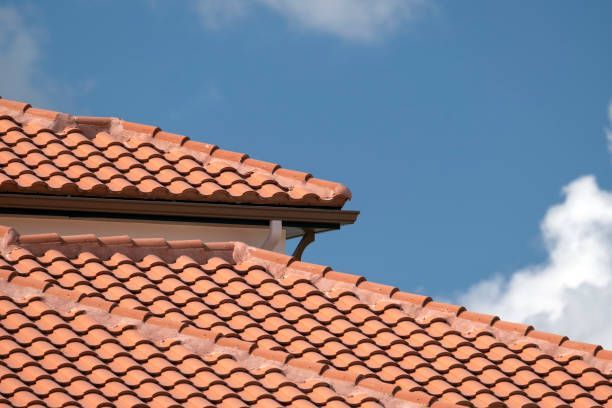 Red tile roof with a brown gutter against a blue sky with clouds.