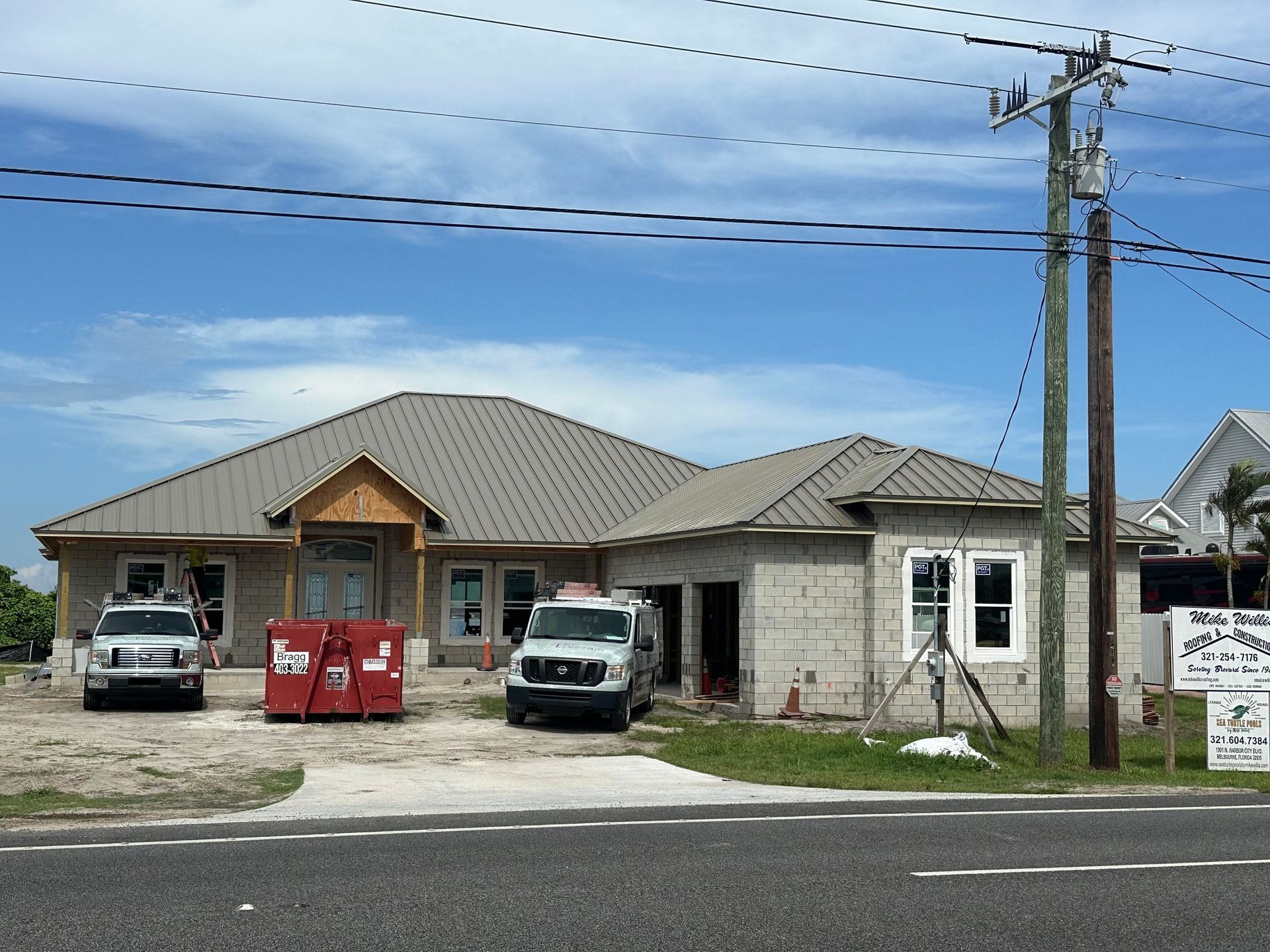 Brown metal roof with dormers and windows on a white building.