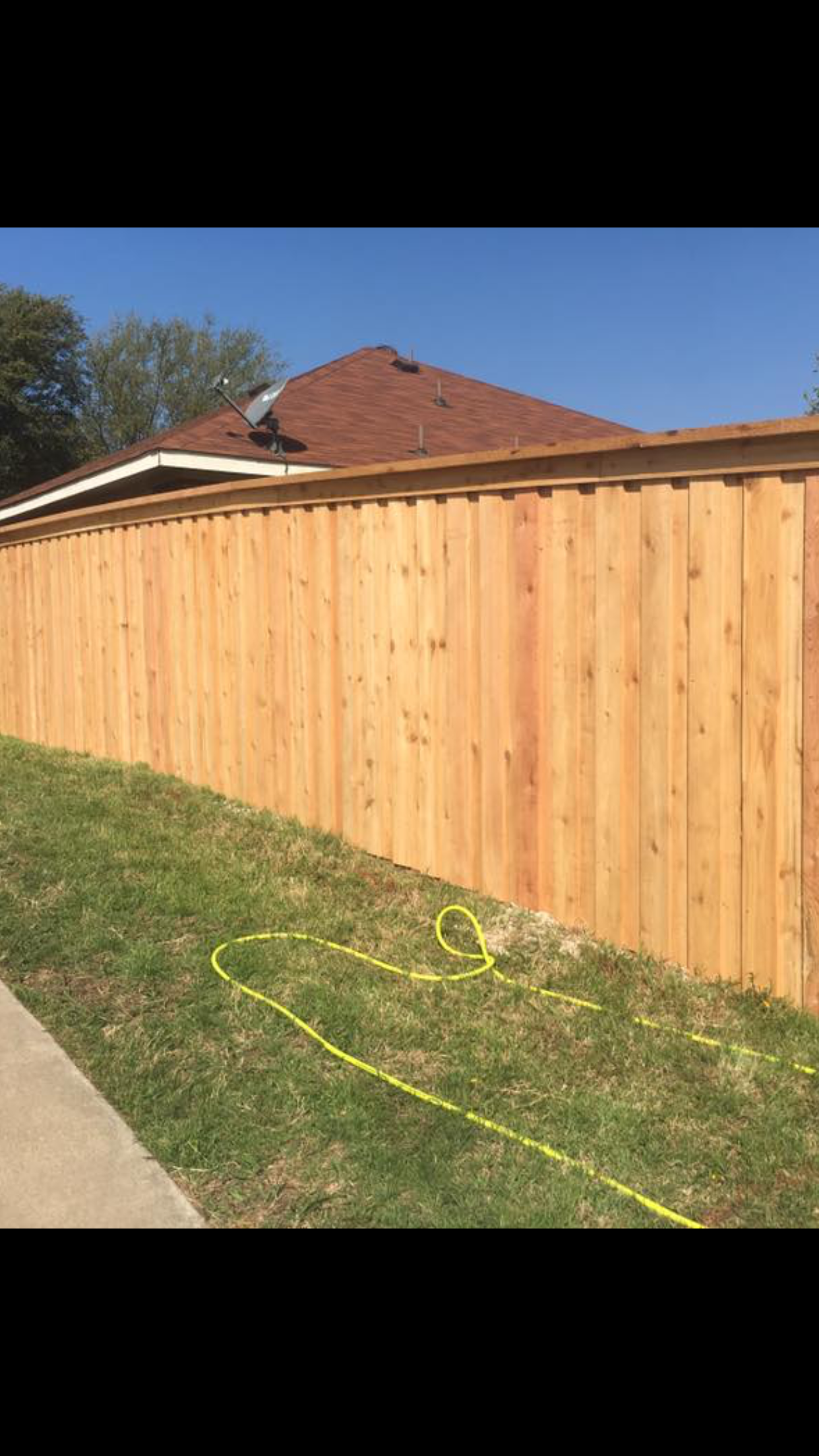 A wooden fence is sitting next to a sidewalk in front of a house.