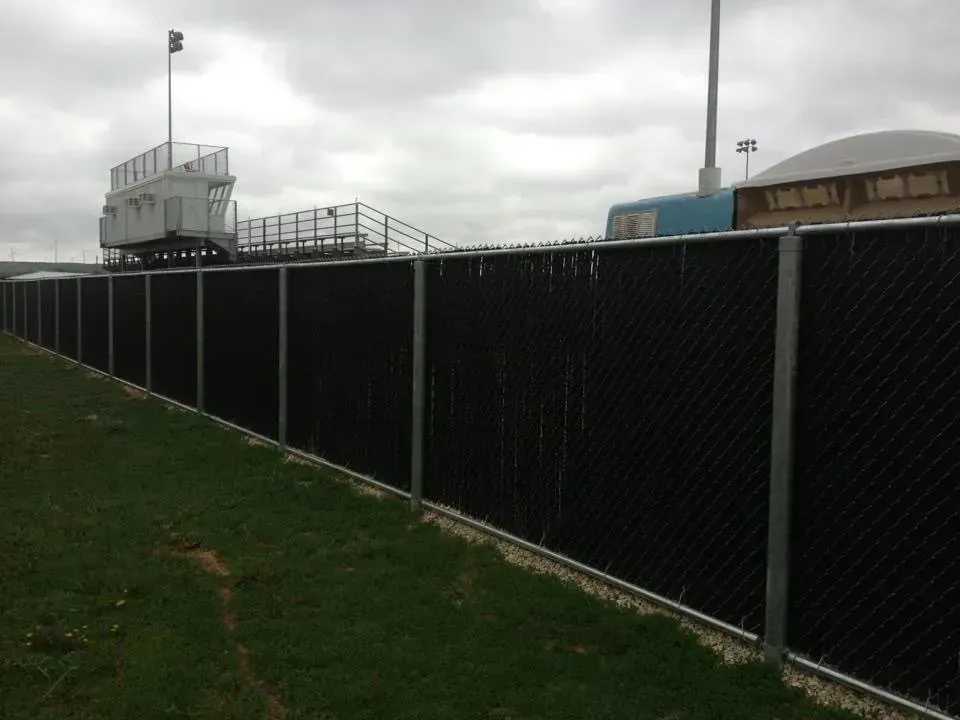A black chain link fence with a stadium in the background