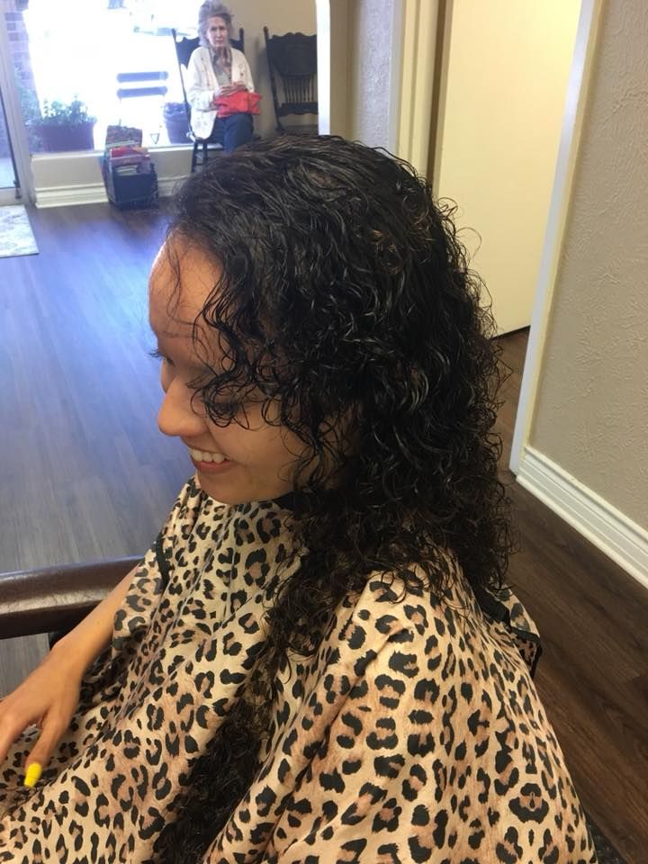 A woman with curly hair is sitting in front of a mirror wearing a leopard print shirt.