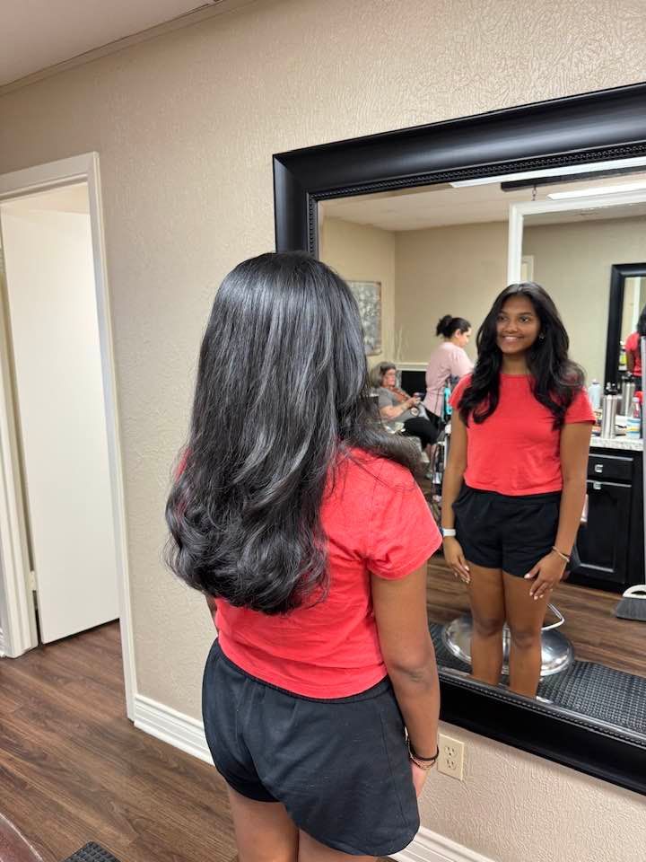 A woman in a red shirt and black shorts is standing in front of a mirror.