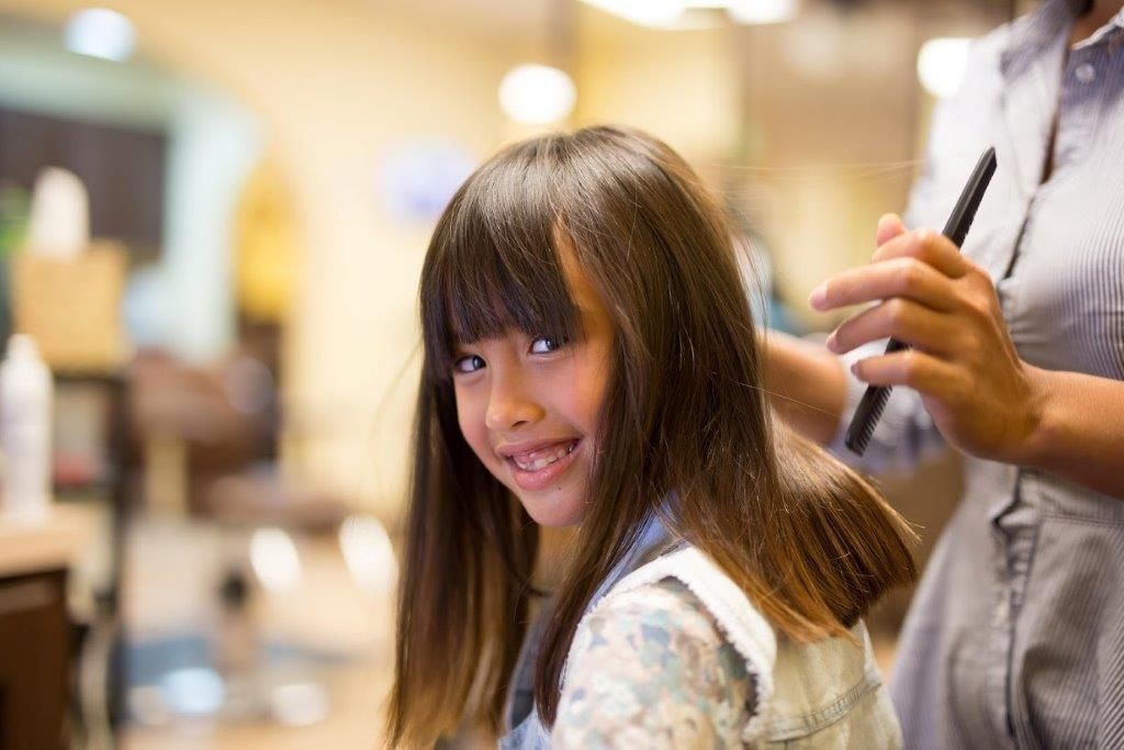 A little girl is getting her hair cut at a hair salon.