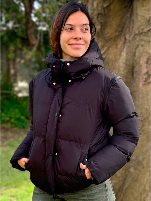 Una mujer que lleva una chaqueta negra con capucha está parada junto a un árbol.