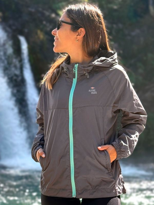 Una mujer que lleva una chaqueta gris está parada frente a una cascada.