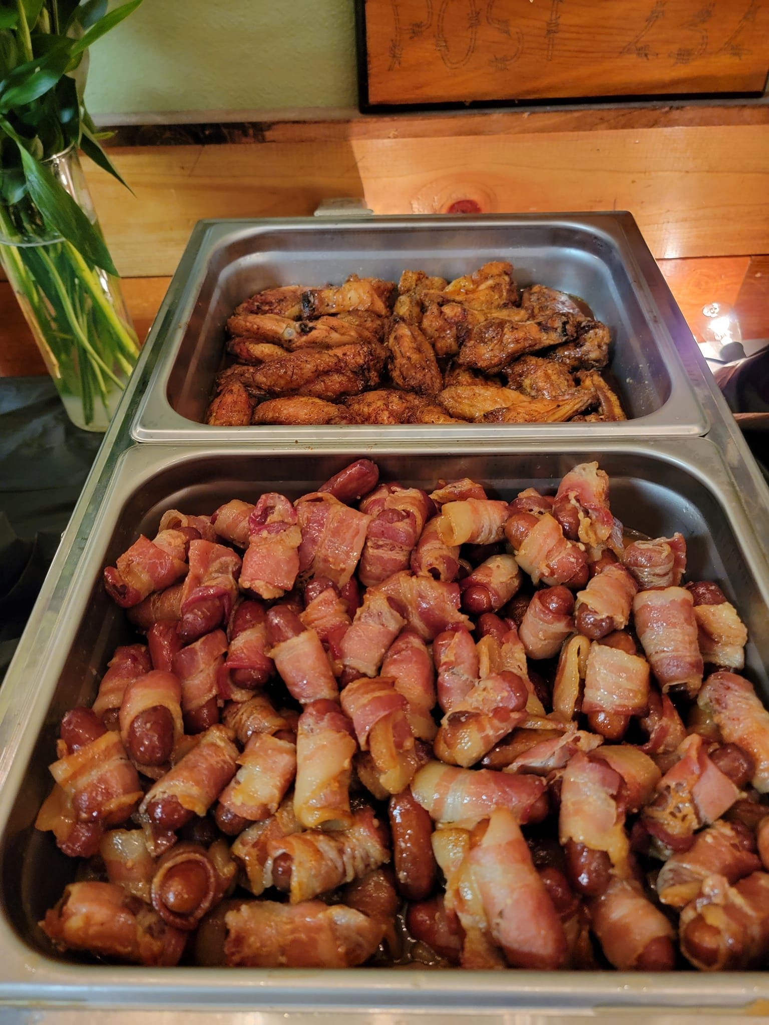 A buffet tray filled with chicken wings and bacon wrapped sausages.