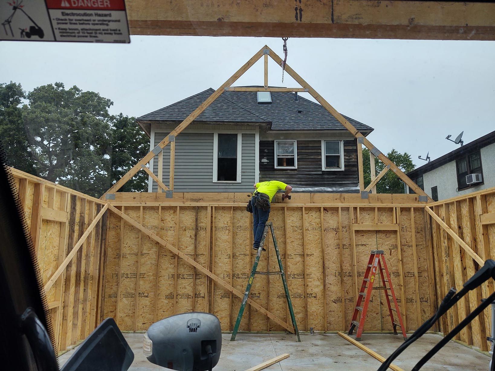 A man is standing on a ladder in front of a house under construction.