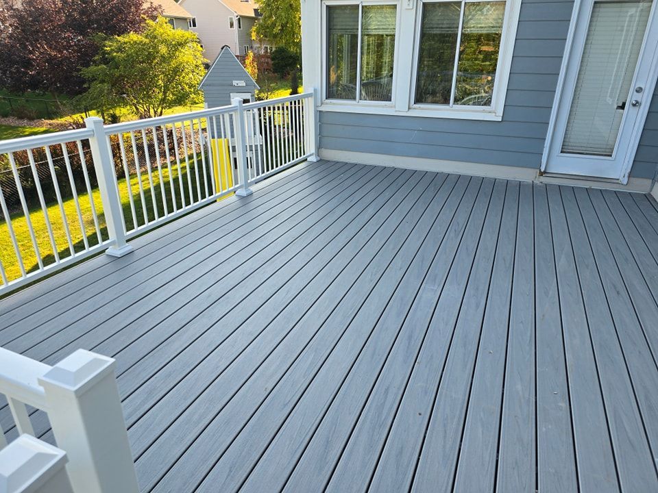 A gray deck with a white railing in front of a house.
