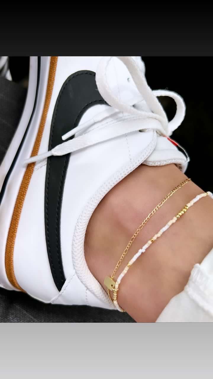 A close up of a person 's ankle wearing an anklet and sneakers.