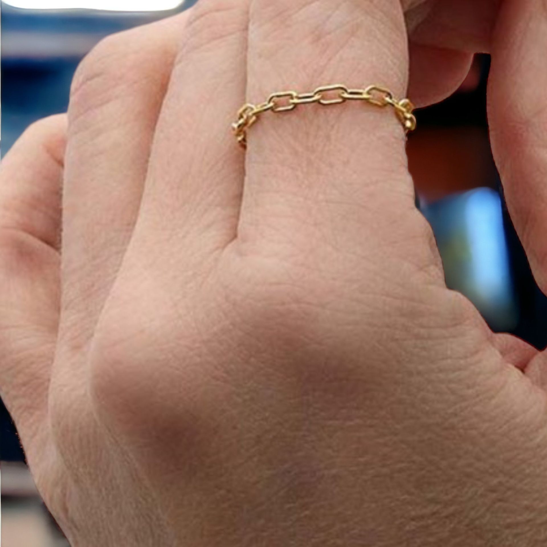 A person wearing a gold chain ring on their finger