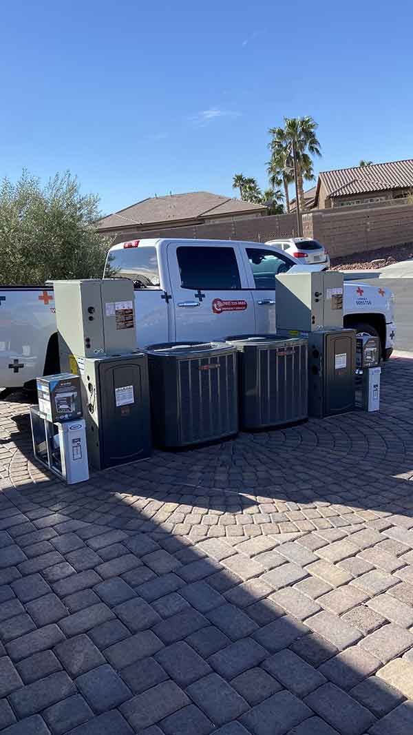 A stack of air conditioners sitting on top of a brick driveway next to a truck.