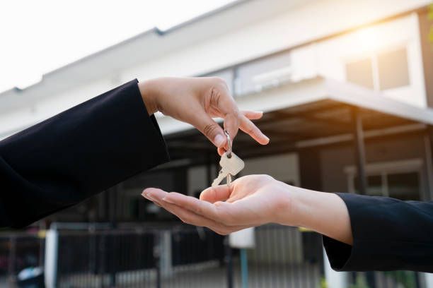 A person is handing a key to another person in front of a house.