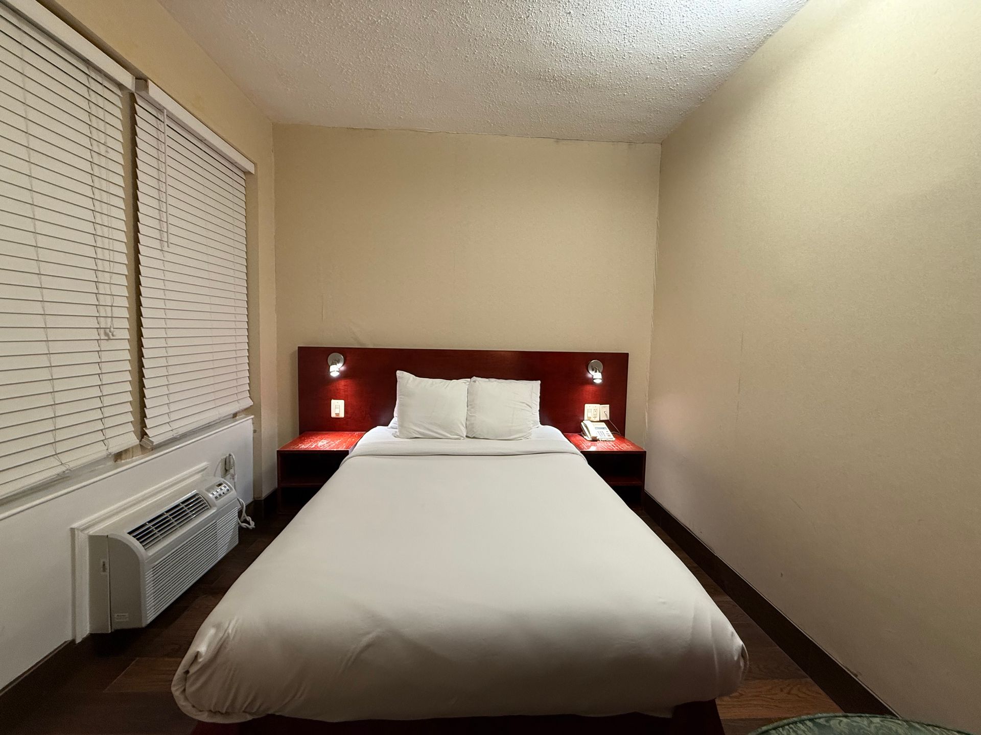 Hotel room with a bed, nightstands, a window with blinds, and an air conditioning unit.