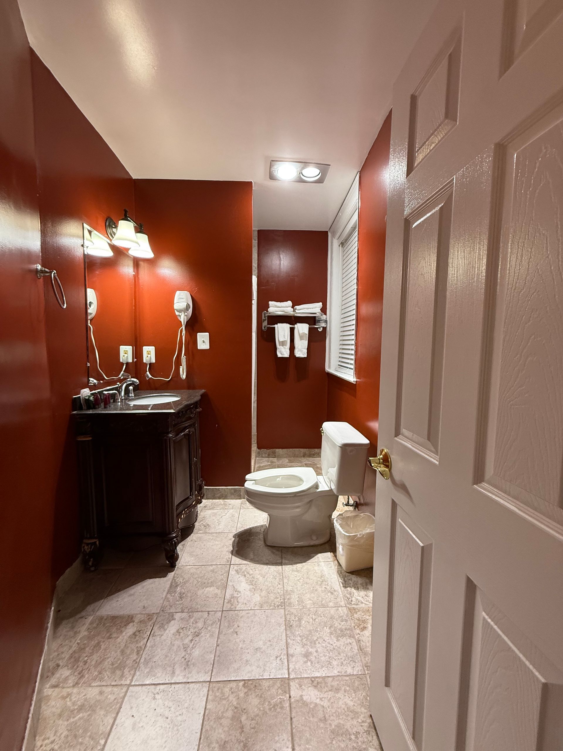 Bathroom with red walls, dark vanity, toilet, and open white door.