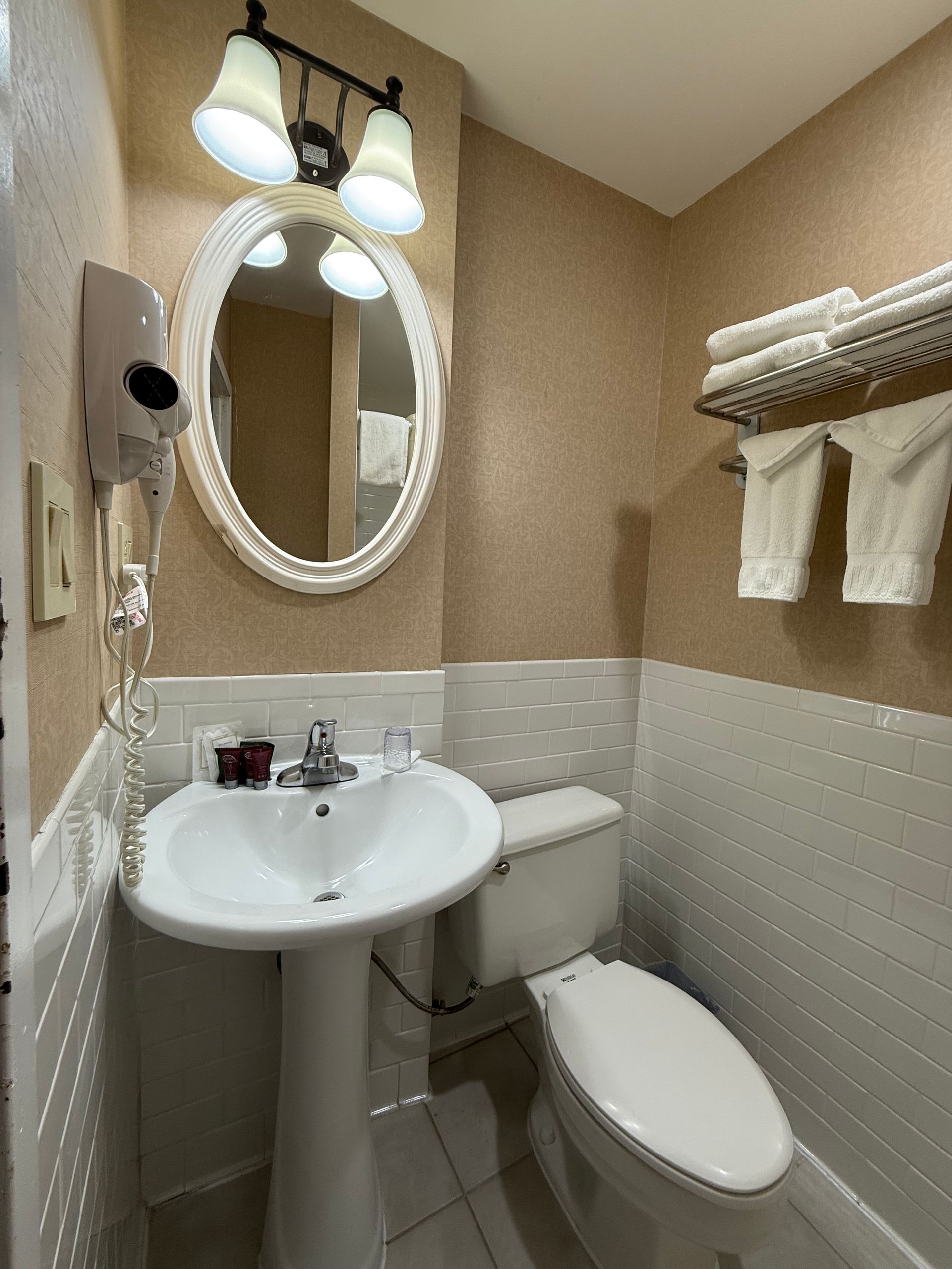Small bathroom with pedestal sink, toilet, oval mirror, and towel rack. Walls are textured.