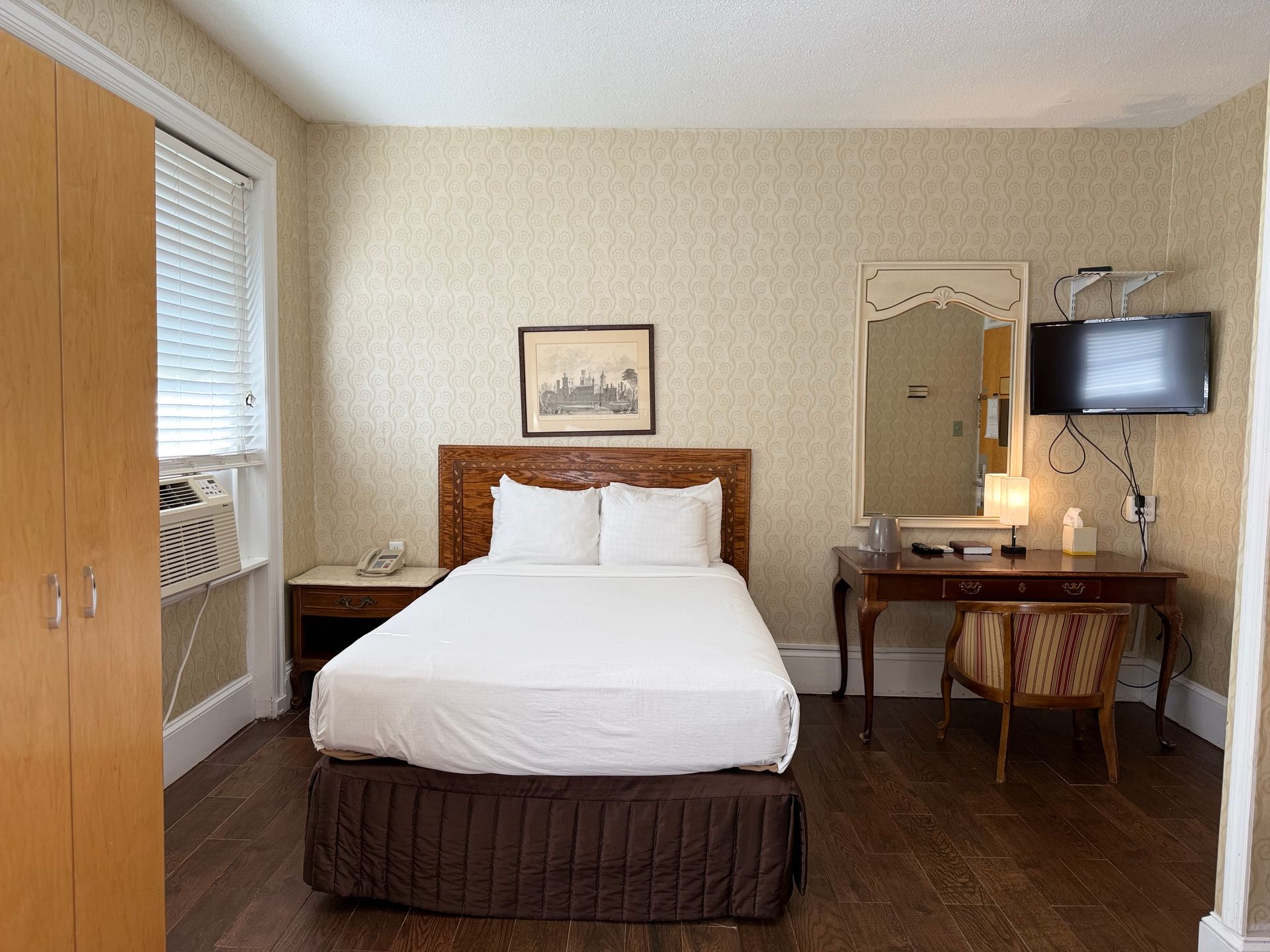 Hotel room with bed, desk, mirror, closet, and window with blinds.