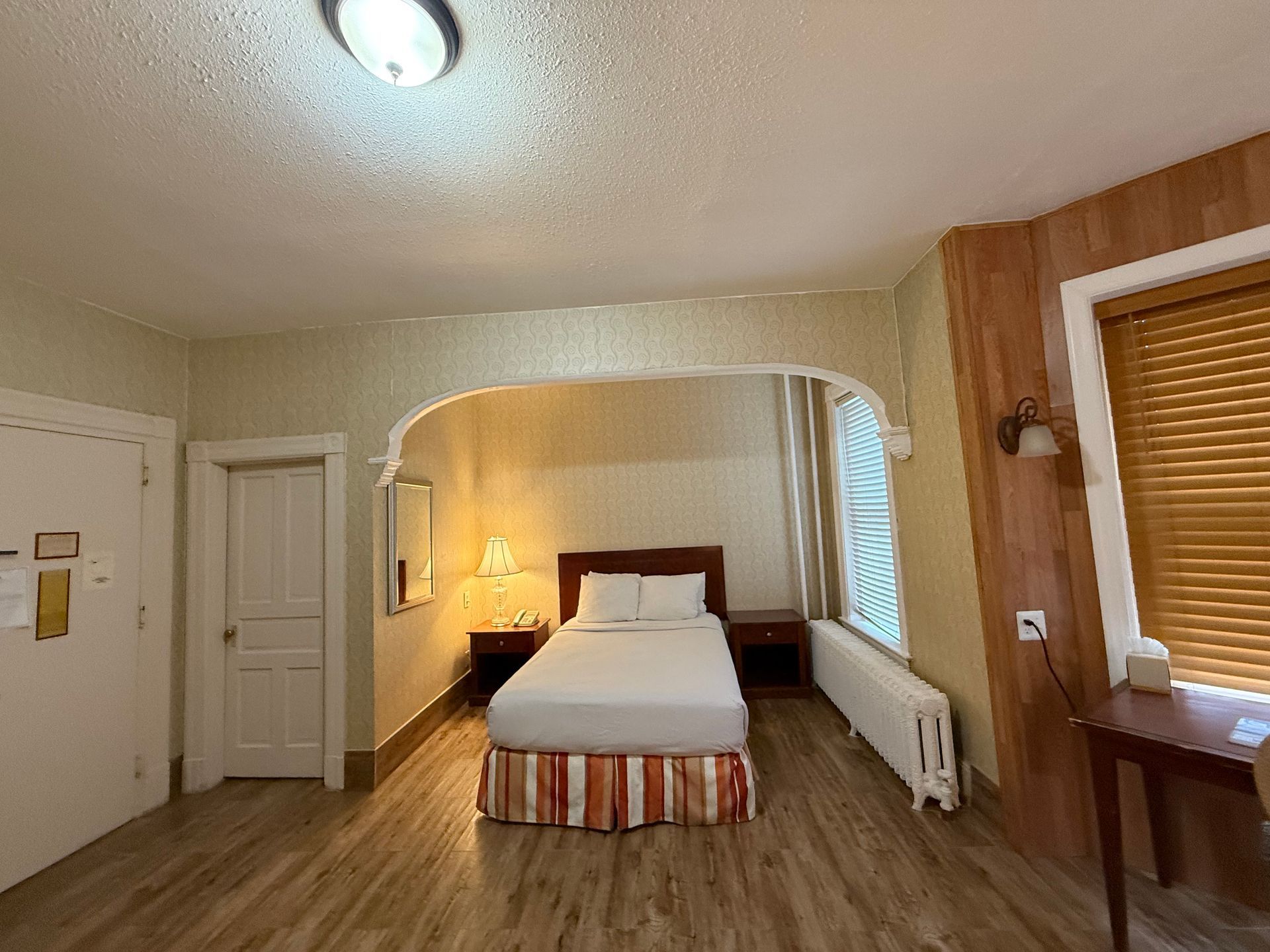 Hotel room with bed, bedside tables, window, and wood paneling.