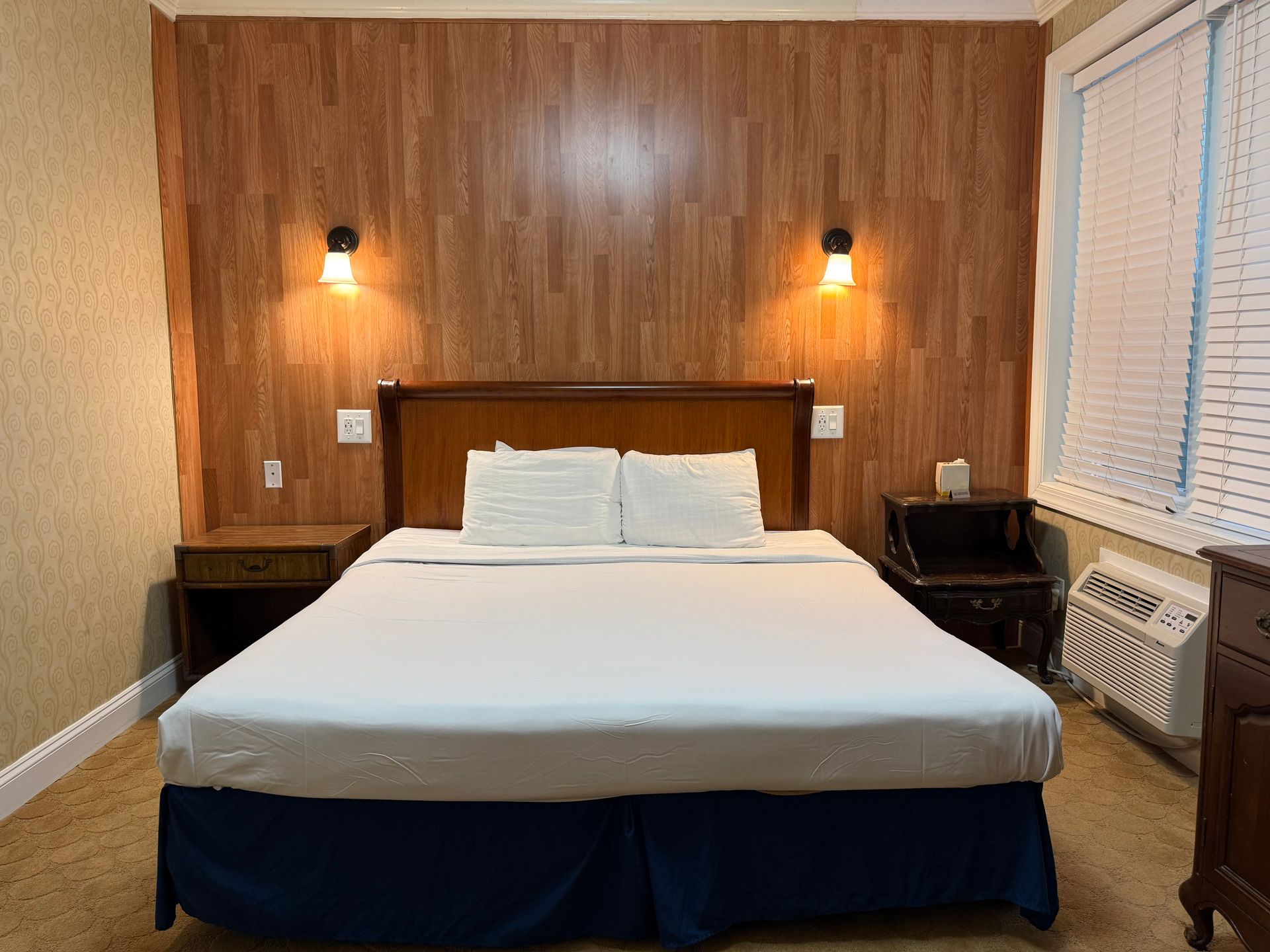 Bedroom with a bed, wood-paneled wall, bedside tables, and two wall-mounted lights.