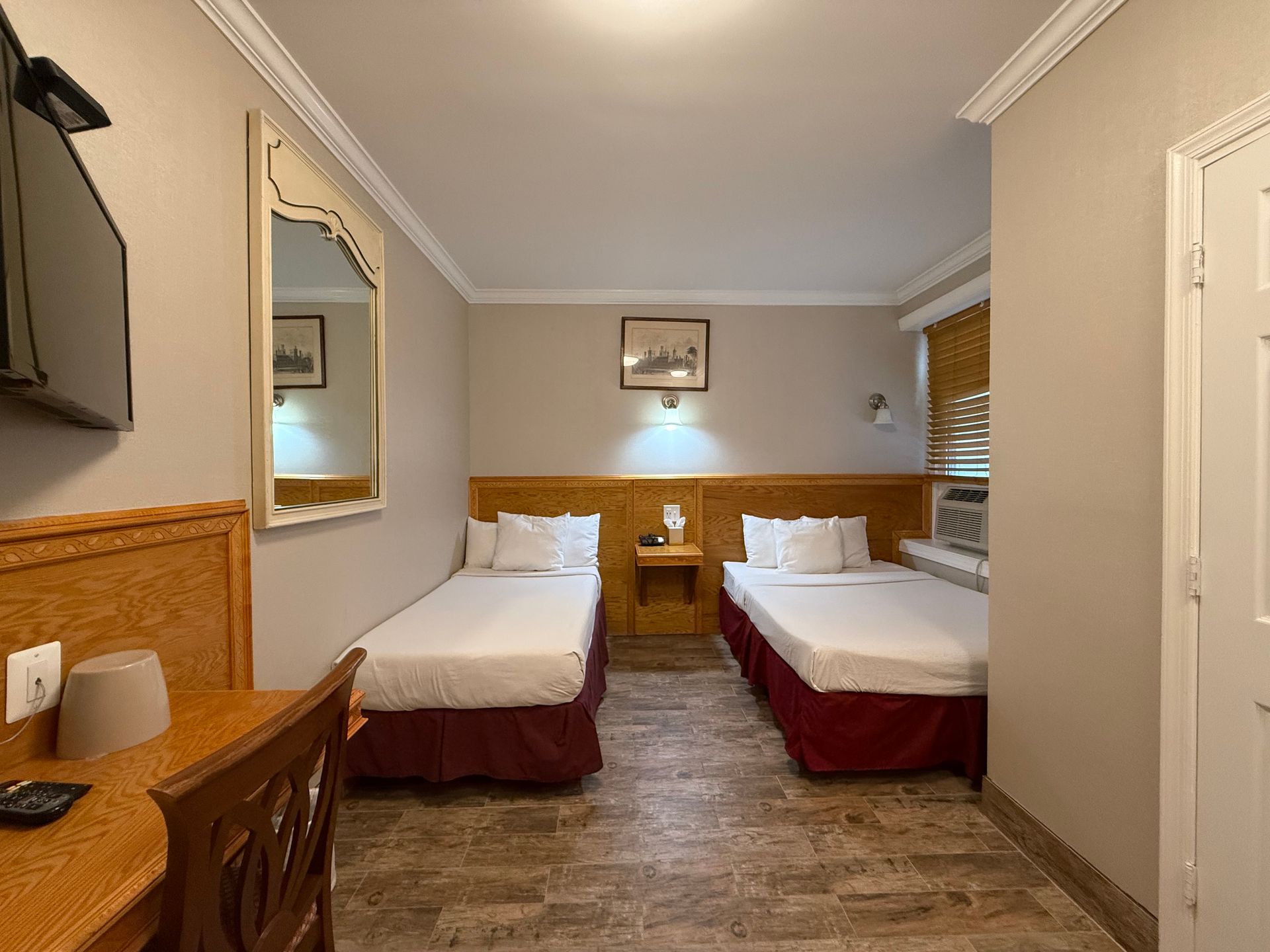 Hotel room with two twin beds, small desk, mirror, and a wall-mounted TV.