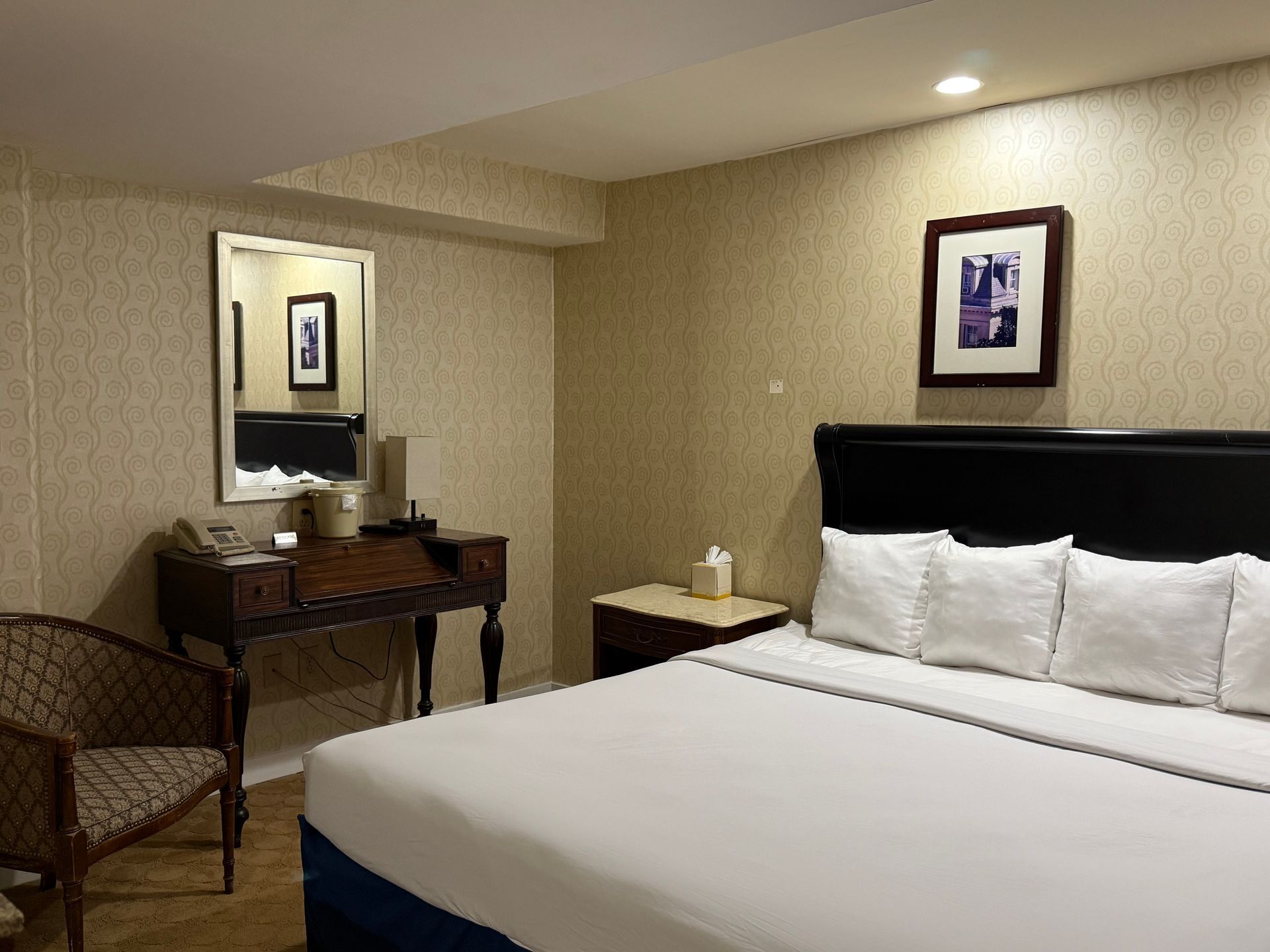 Hotel room with a bed, desk, chair, and framed artwork on the wall.