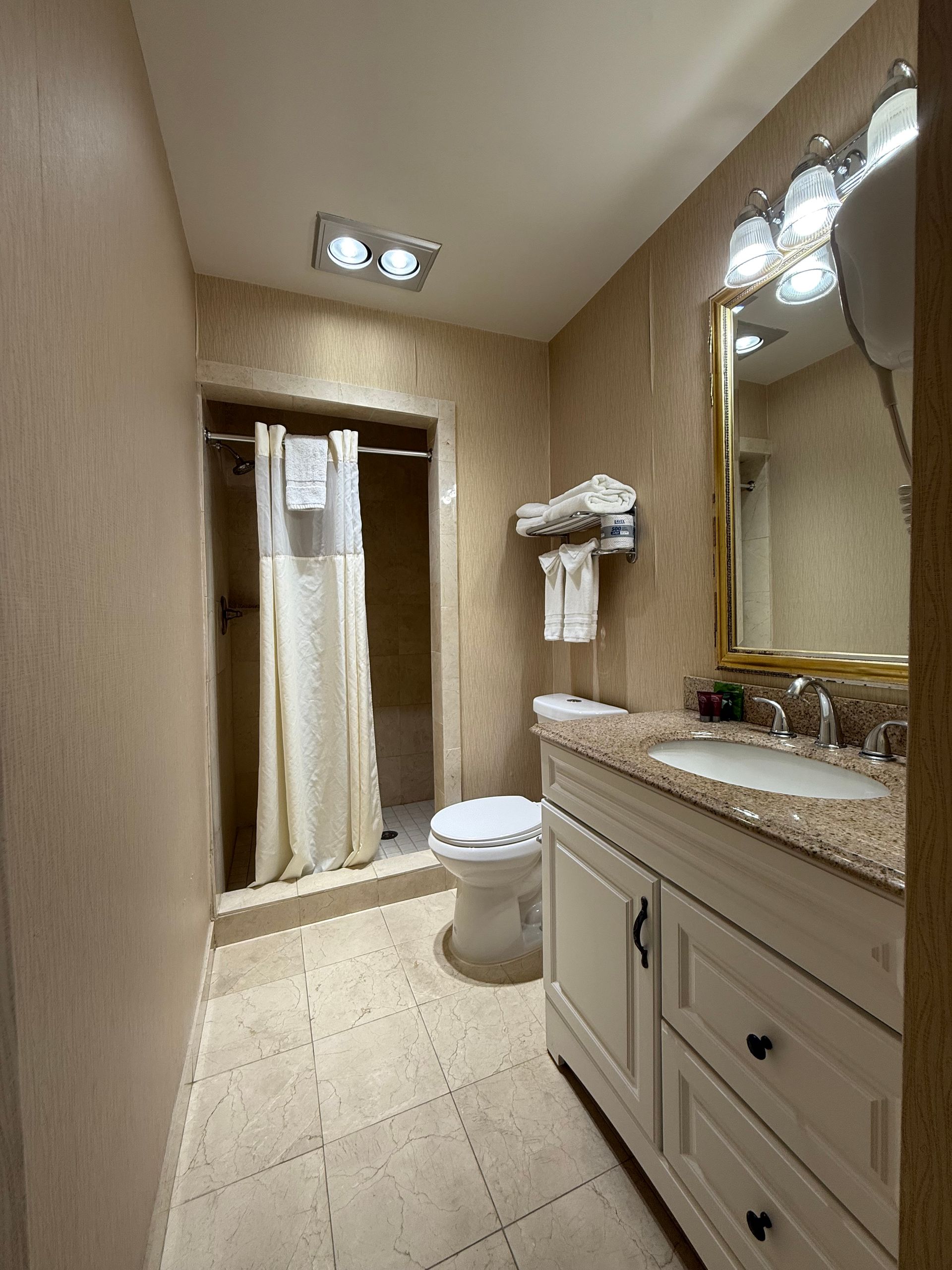 Bathroom with shower, toilet, vanity, and beige textured walls.