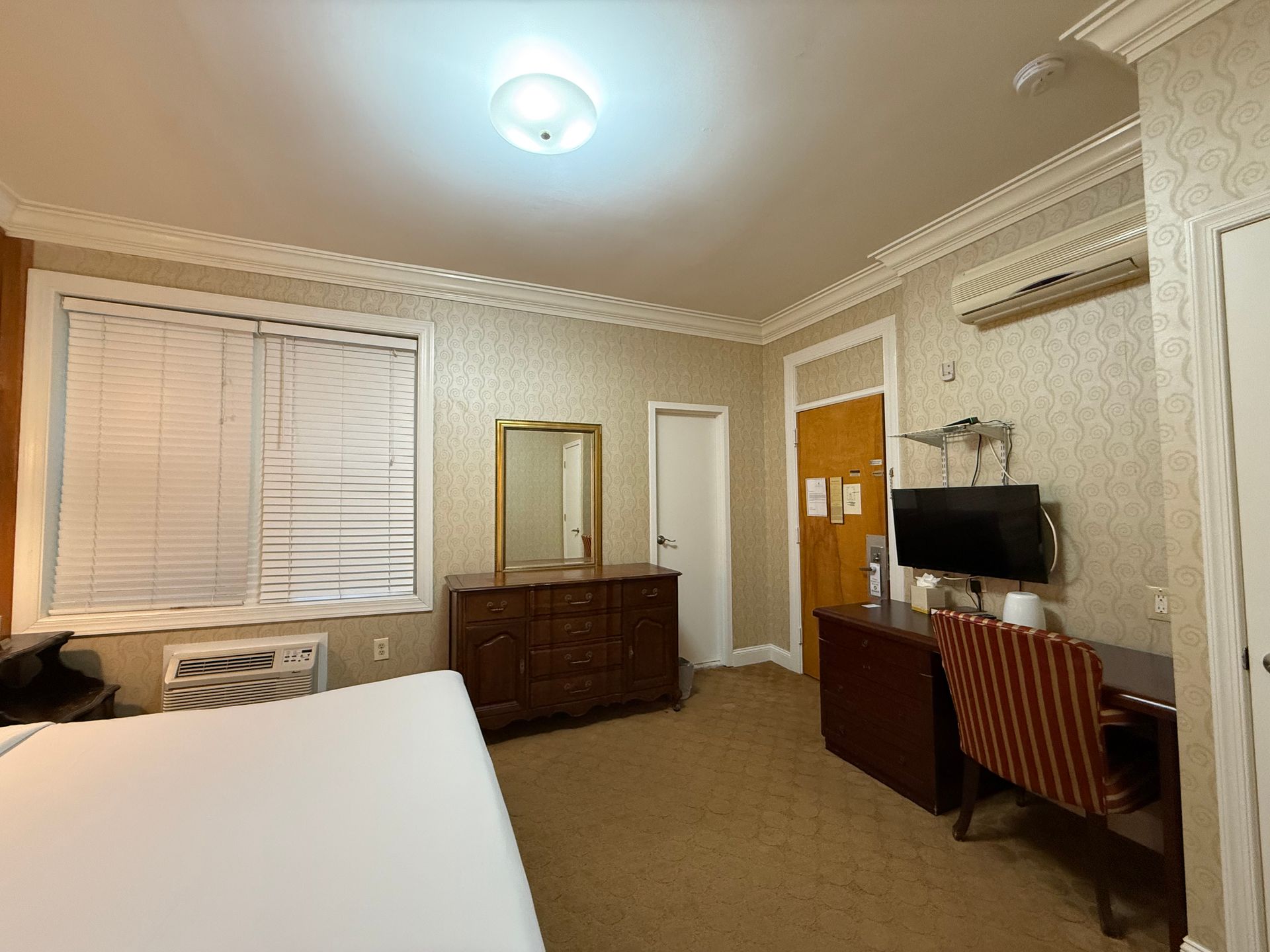 Hotel room with a bed, dresser, TV, and window with blinds.