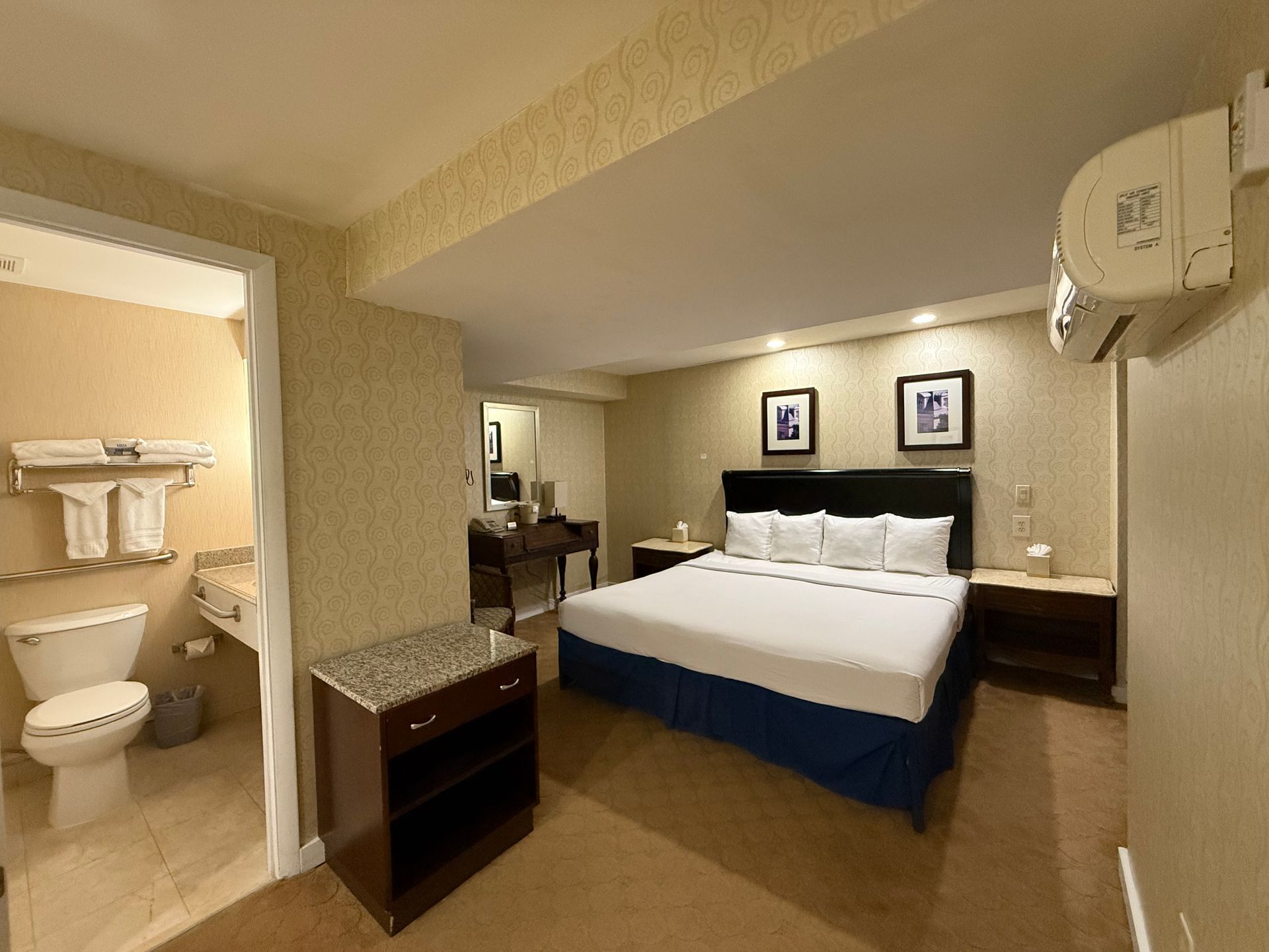 Hotel room interior with a king-size bed, bathroom on the left, and a dresser in front.