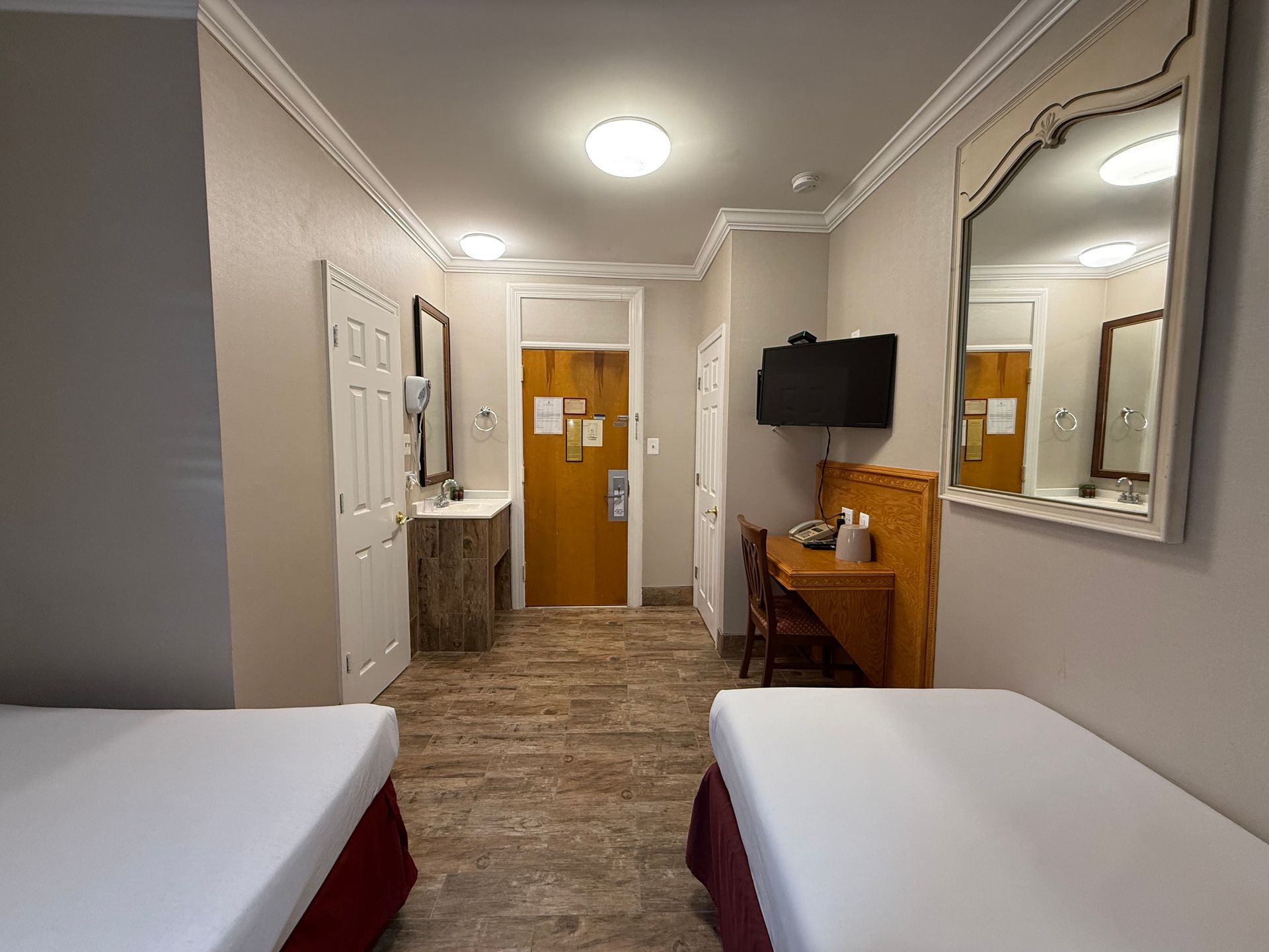 Hotel room with two beds, desk, mirror, and bathroom entrance.