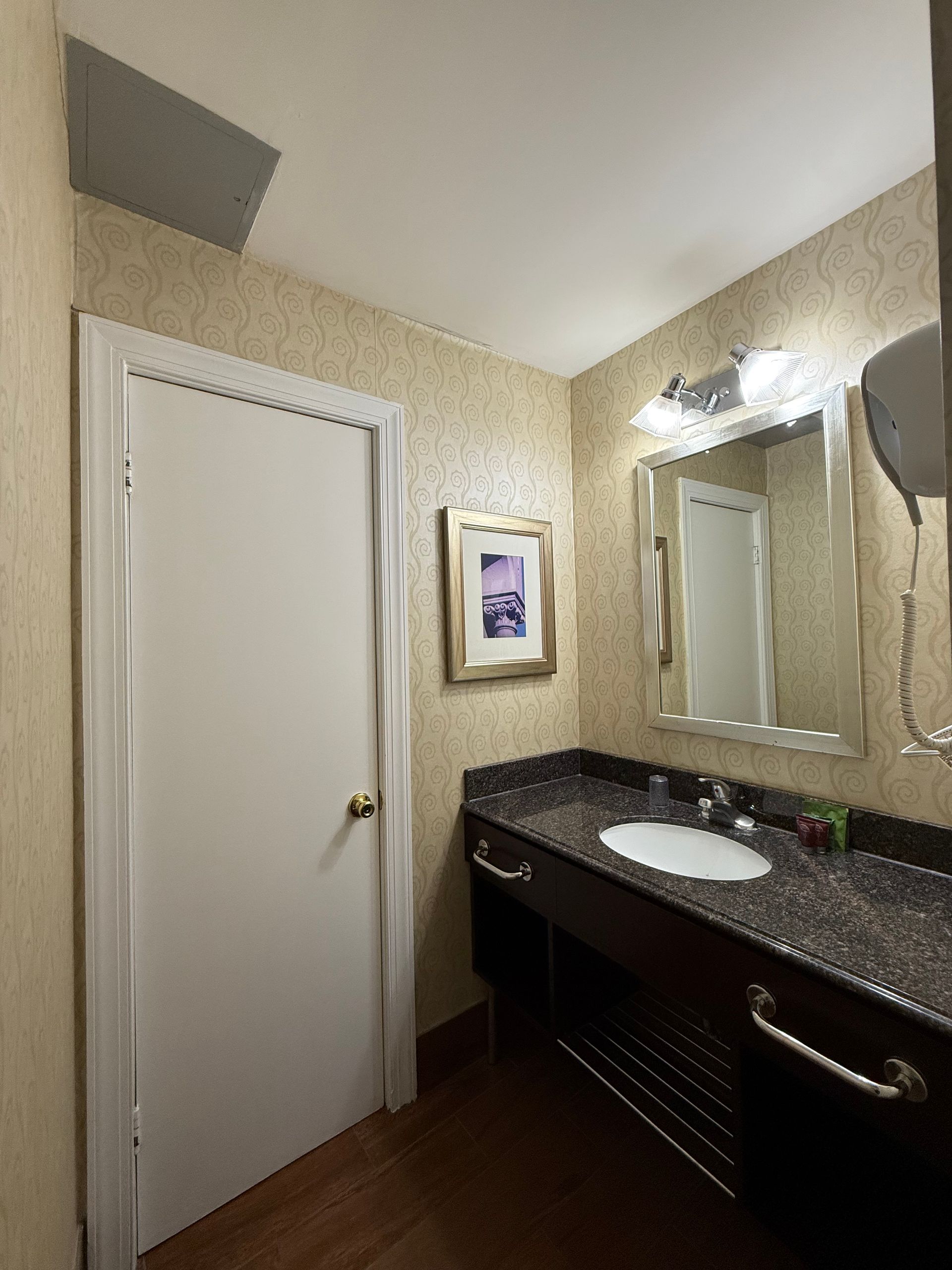 Bathroom with white door, dark vanity, mirror, and a small framed picture on textured wallpaper.