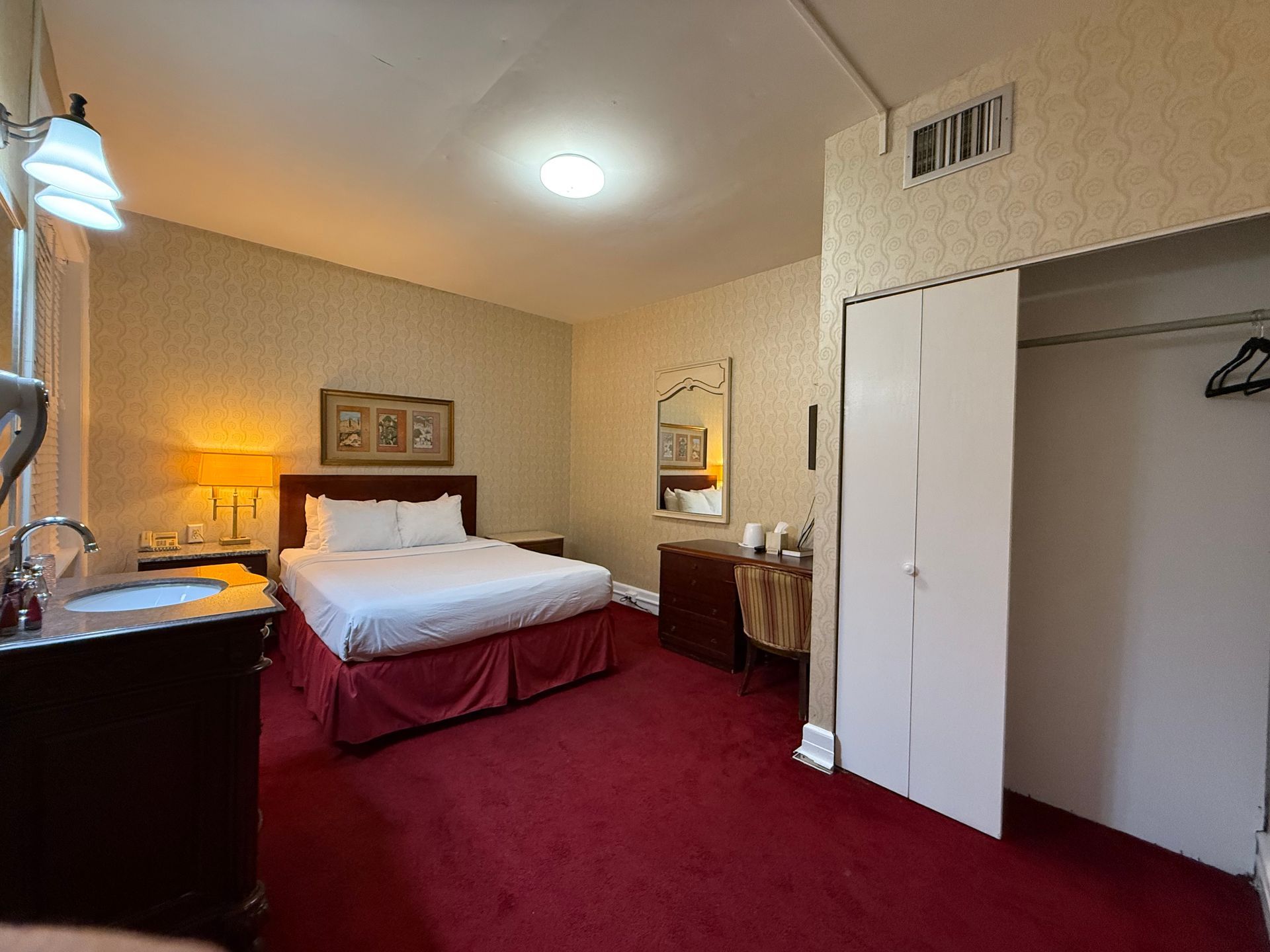 Hotel room with a bed, desk, red carpet, and a closet.