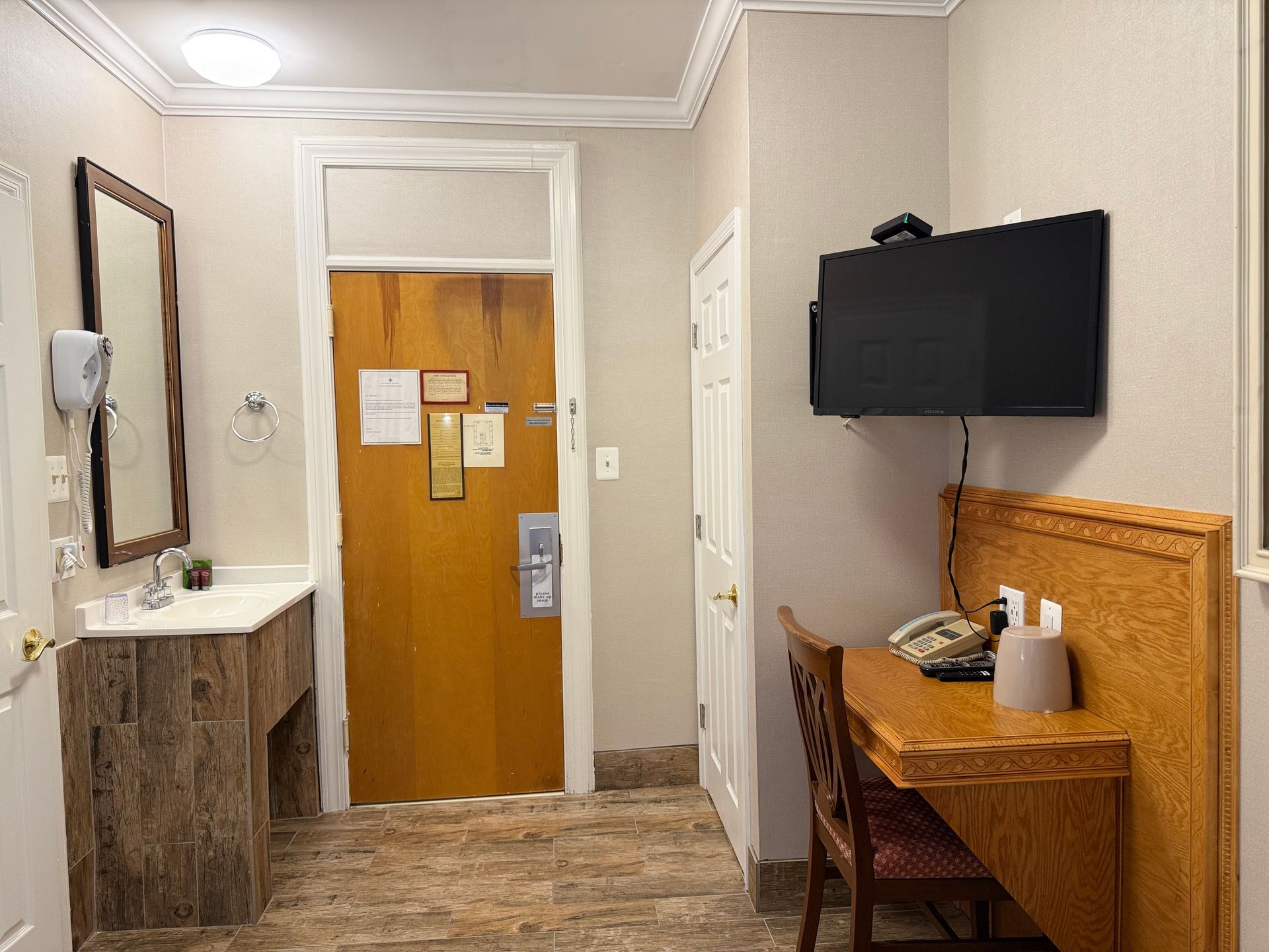 Hotel room interior: sink, door, desk with TV above.
