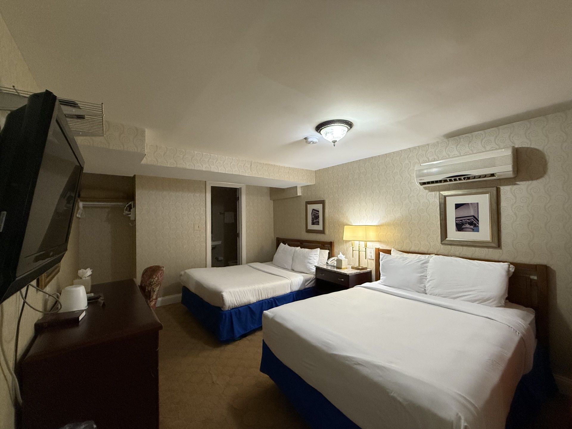 A hotel room with two beds, a TV, a desk, and a window.