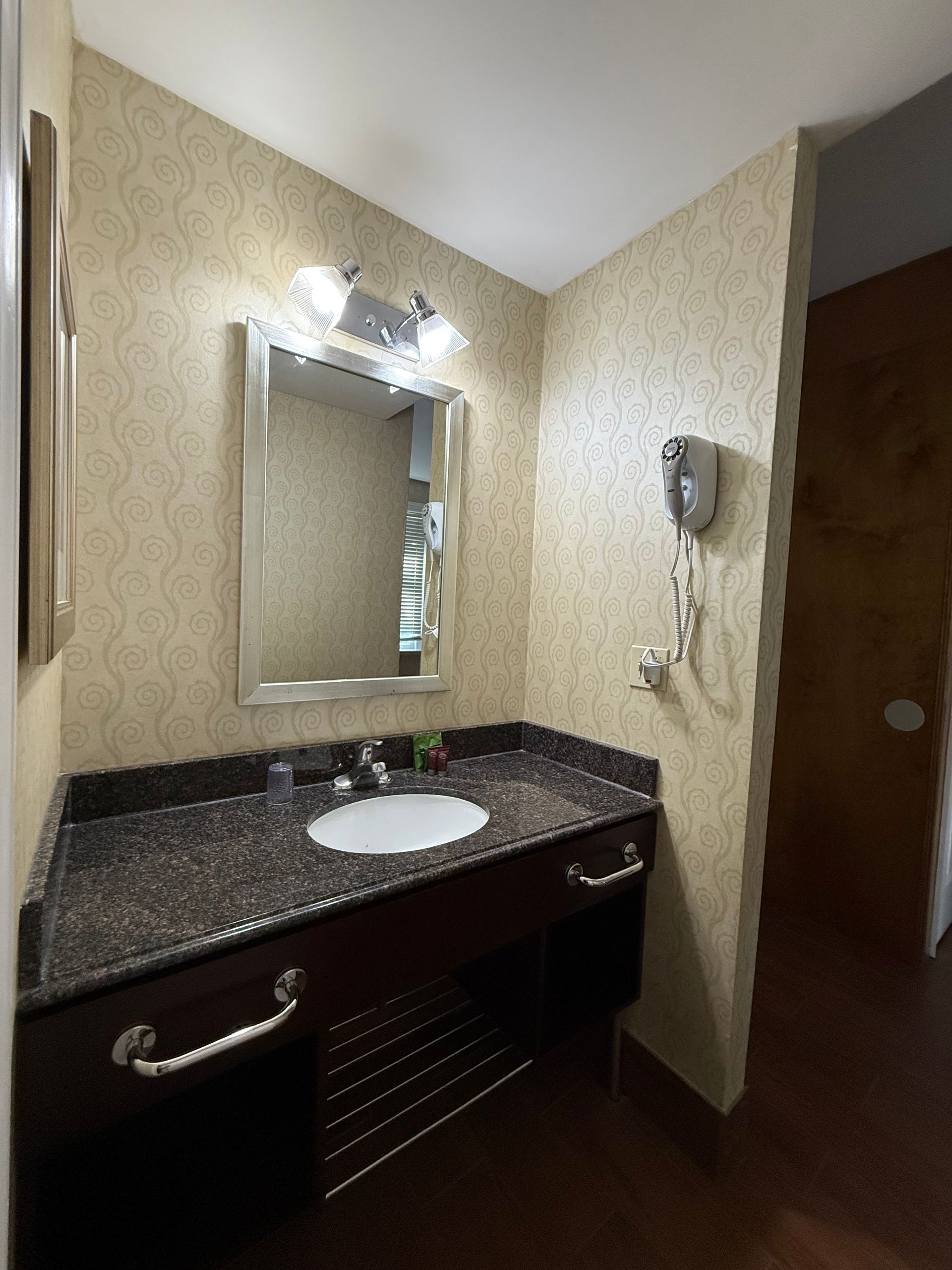 Bathroom with a dark countertop sink, mirror, and a hair dryer on the wall.