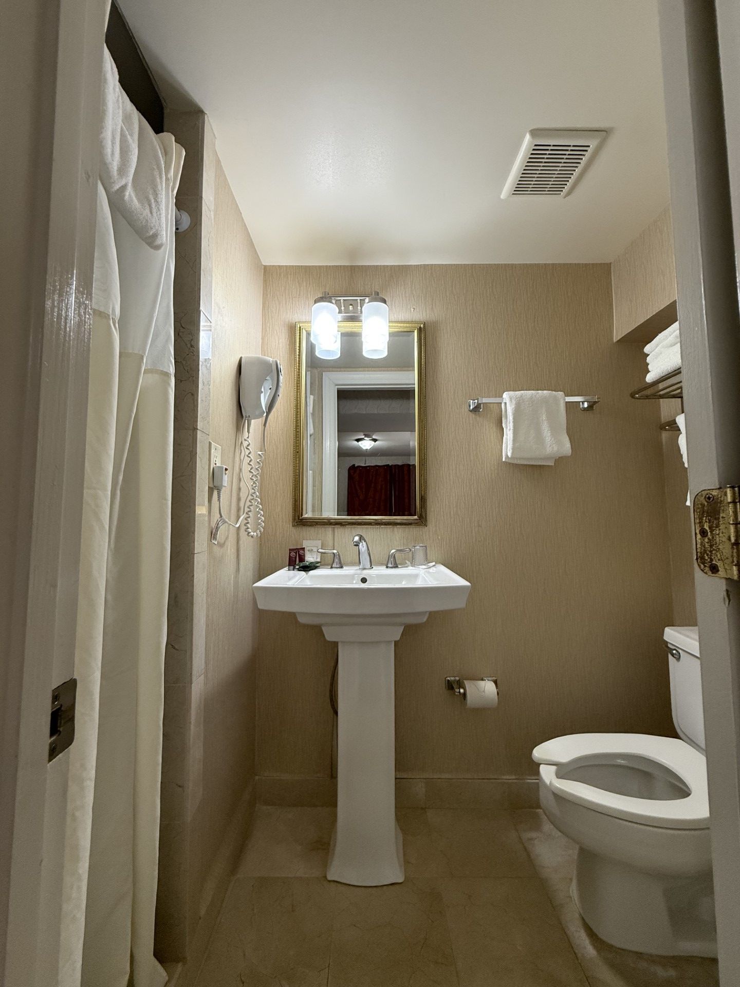 Bathroom with a pedestal sink, toilet, mirror, towel rack, and shower curtain. Beige walls and floor.