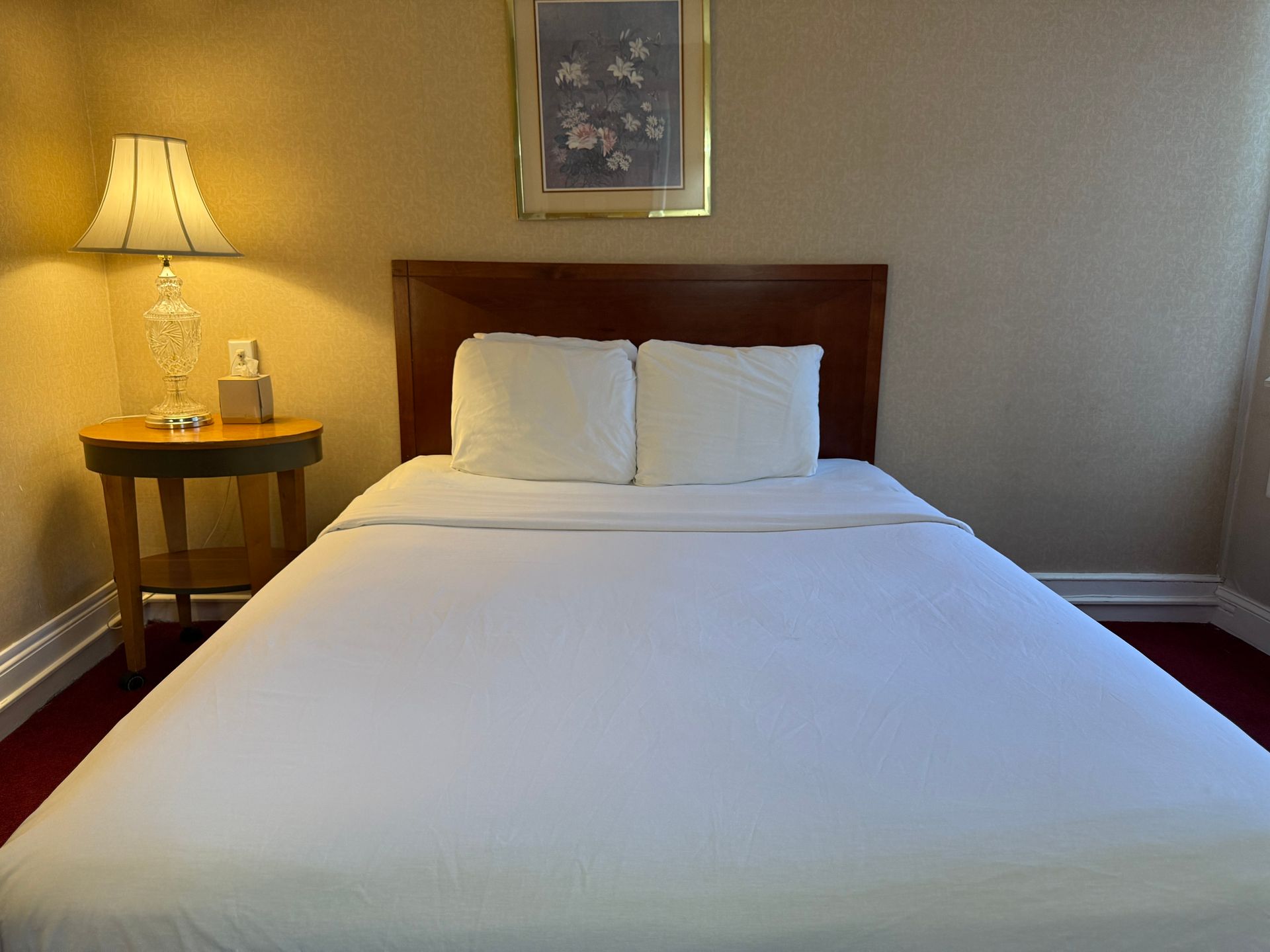 A neatly made bed with white linens, flanked by a lamp and a small table in a hotel room.