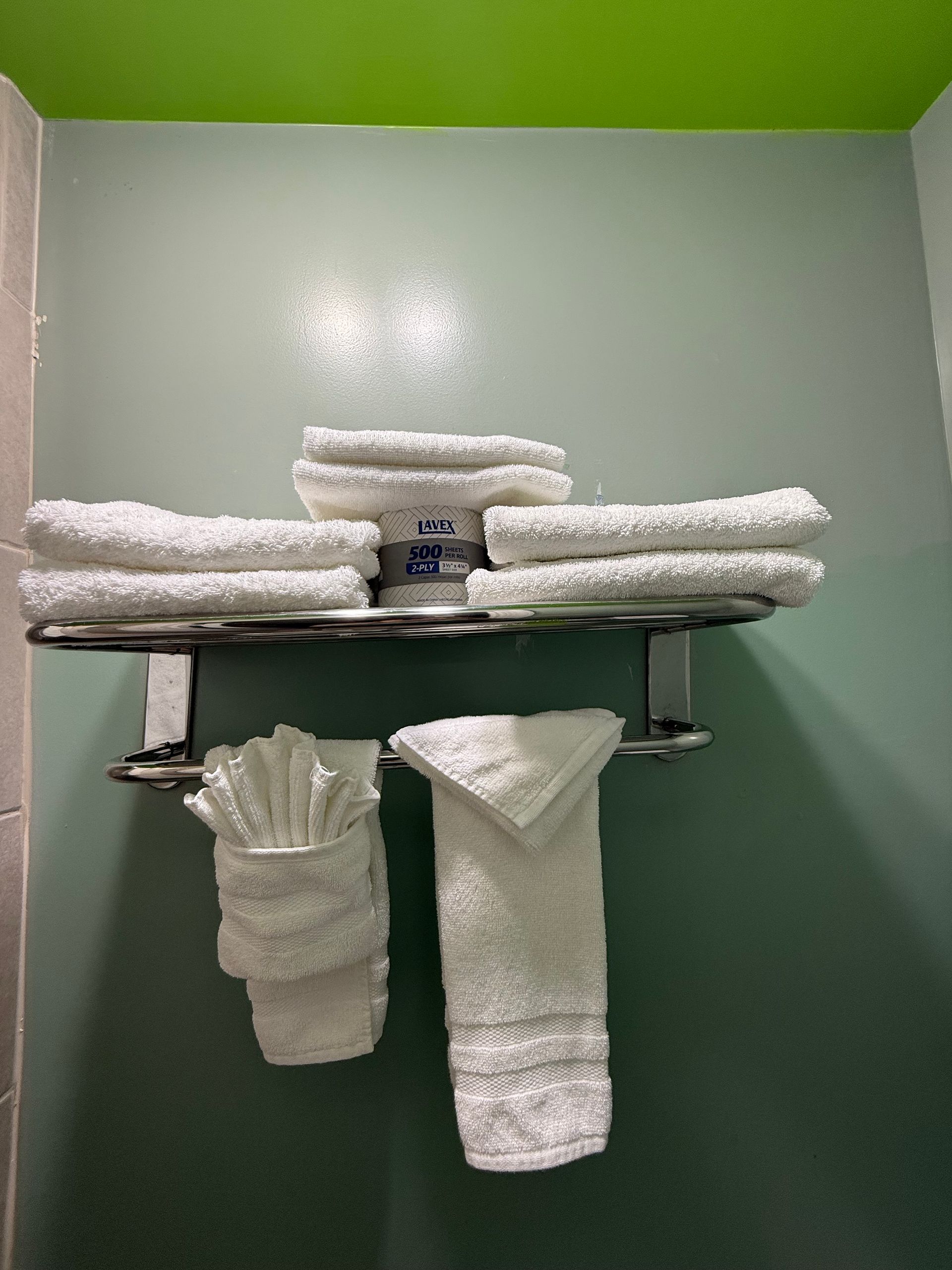 White towels stacked on a metal rack against a green wall. Two towels hang below.