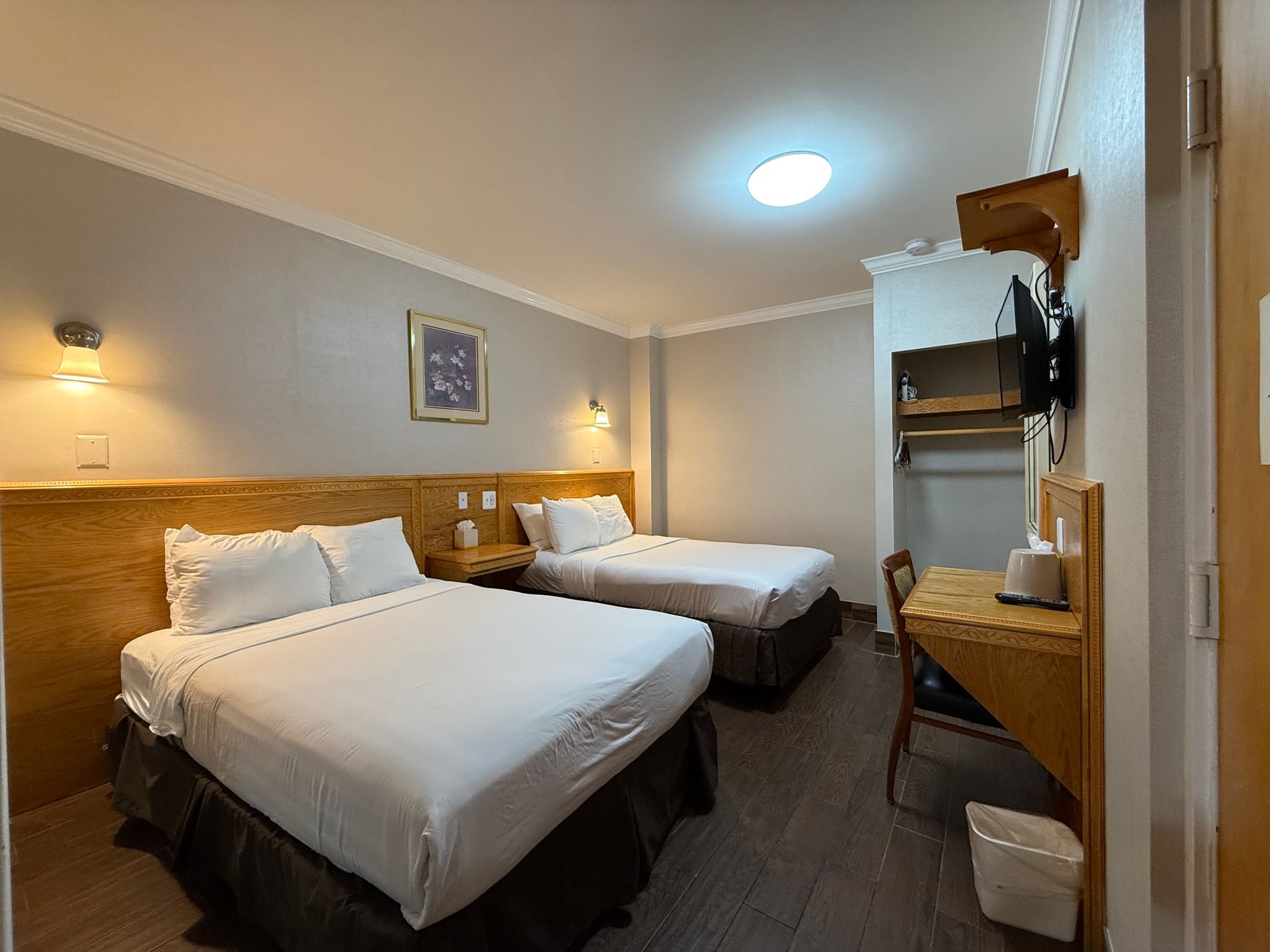 Hotel room with two beds, nightstand, desk, and TV. Gray walls, wooden bed frames and trim.