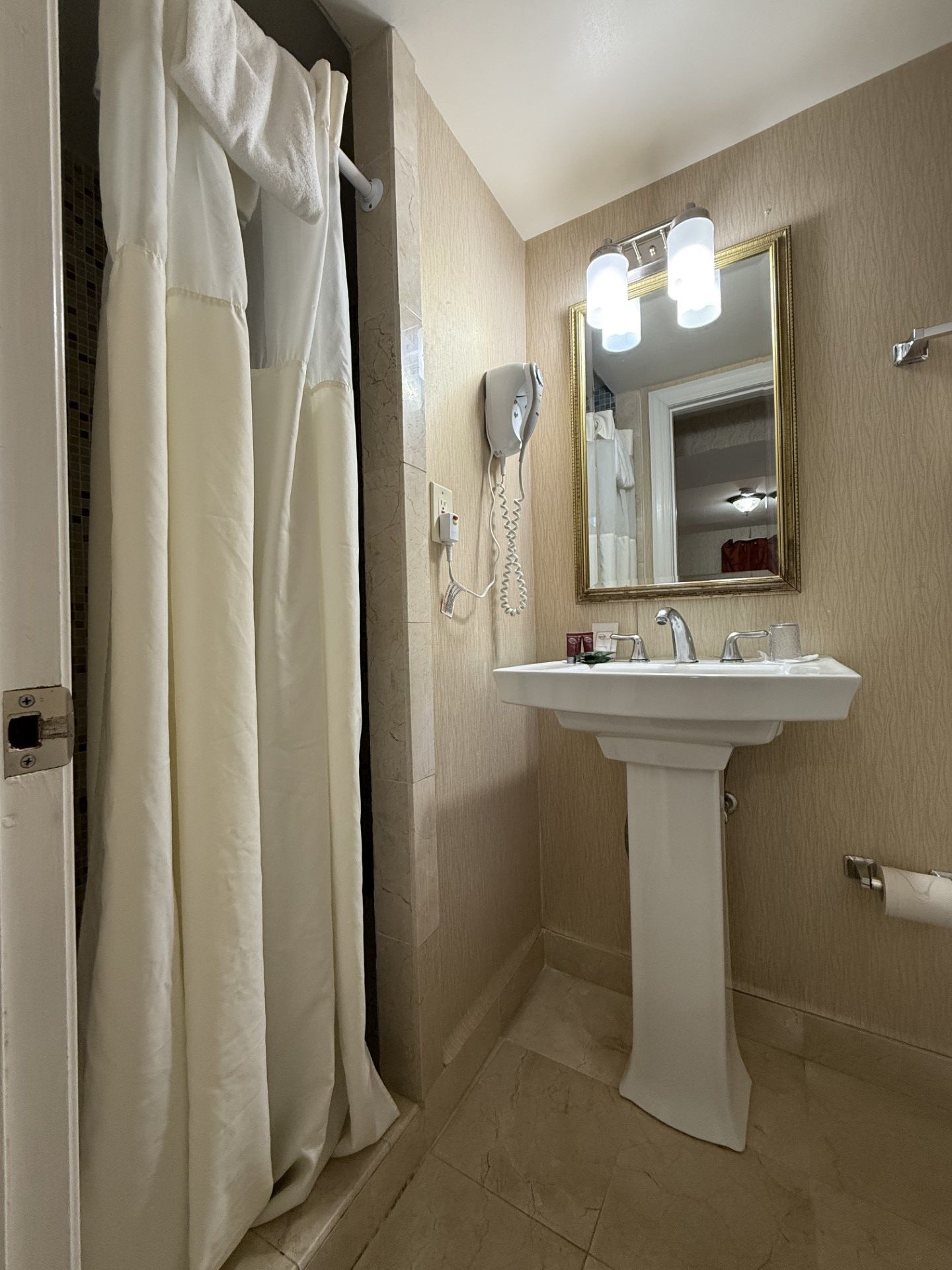 Bathroom with shower, pedestal sink, mirror, and towel rack. Beige walls and floor.