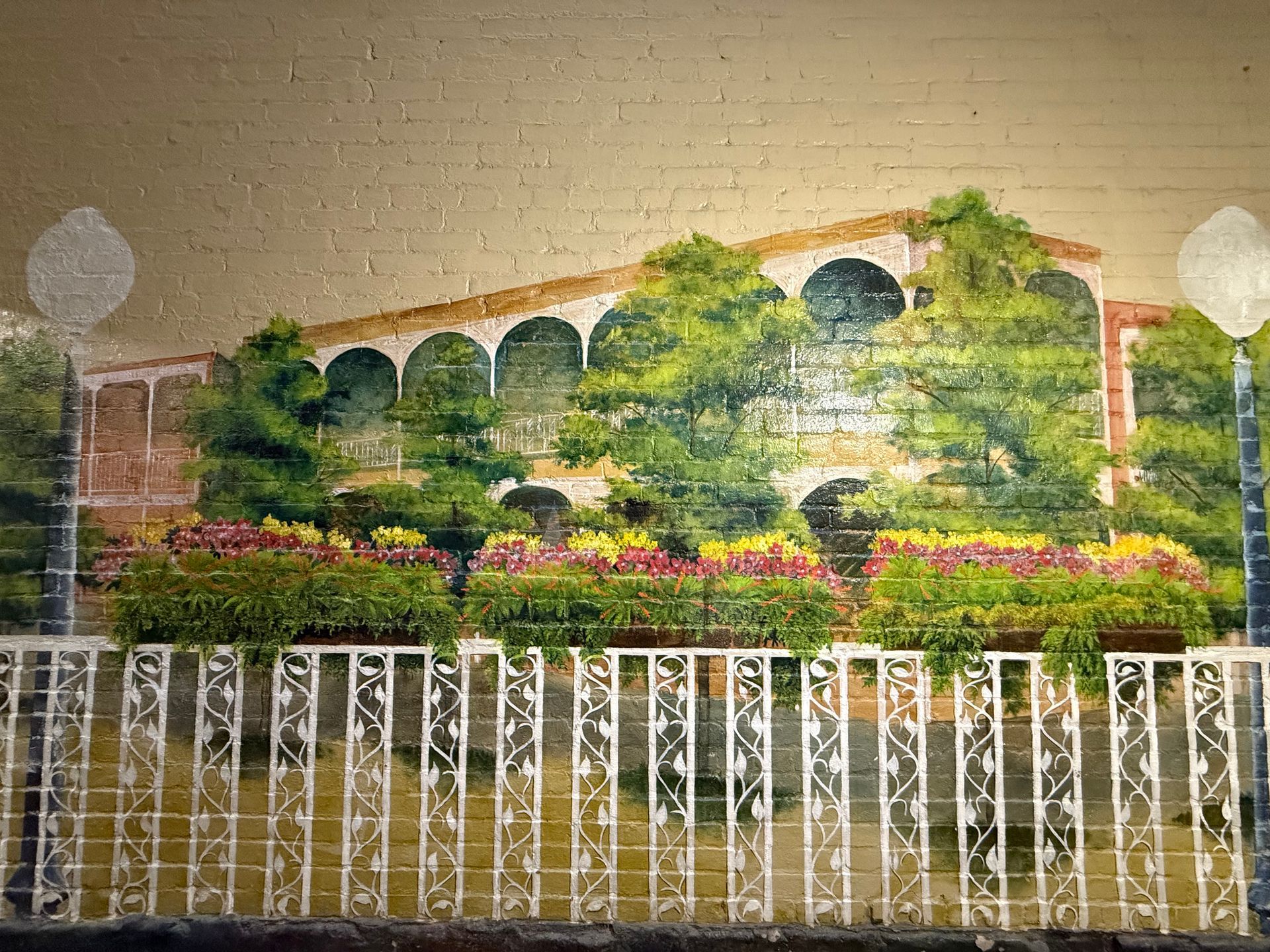 Building with arched windows, surrounded by colorful flowers and greenery, behind a decorative white fence.