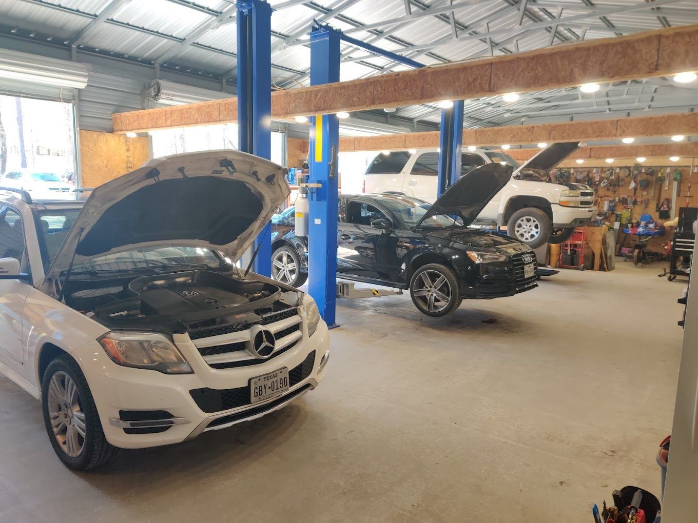 Cars being serviced in an auto repair shop with open hoods, overhead lift, and light-colored floor. | Freedom Auto Repair