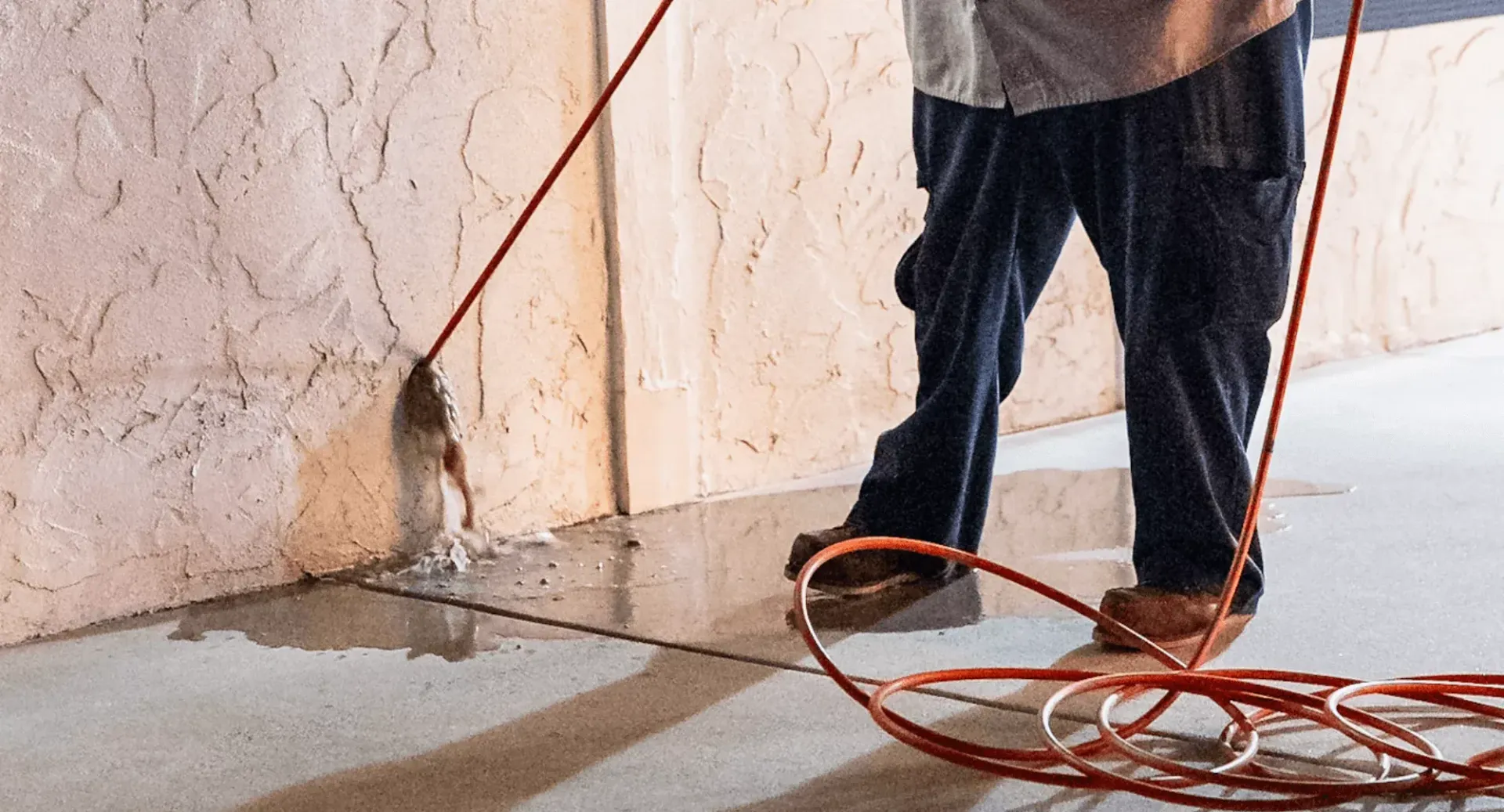 A man is standing next to a wall with a hose.