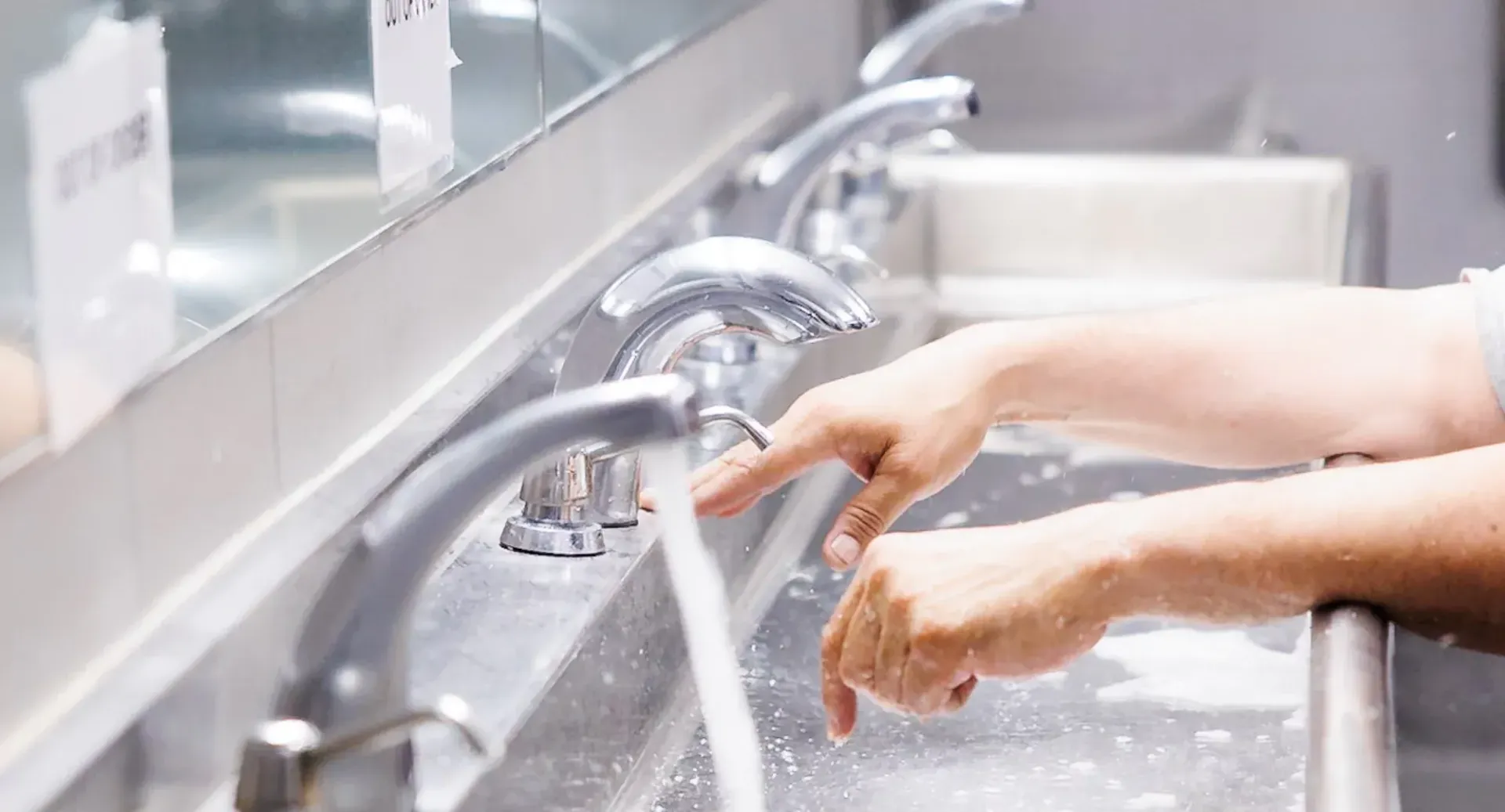 A person is washing their hands in a public bathroom sink.