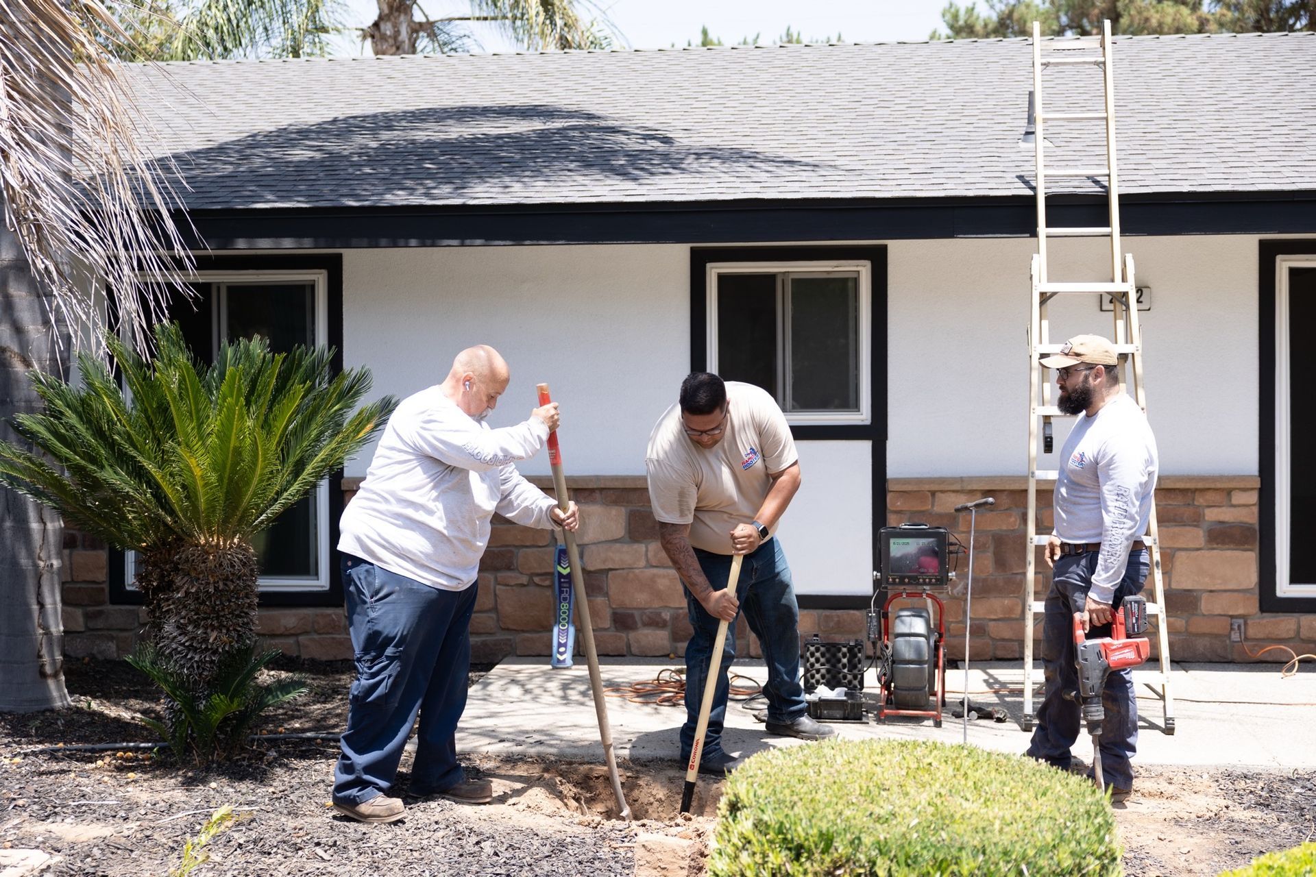 Three men are digging a hole in front of a house.