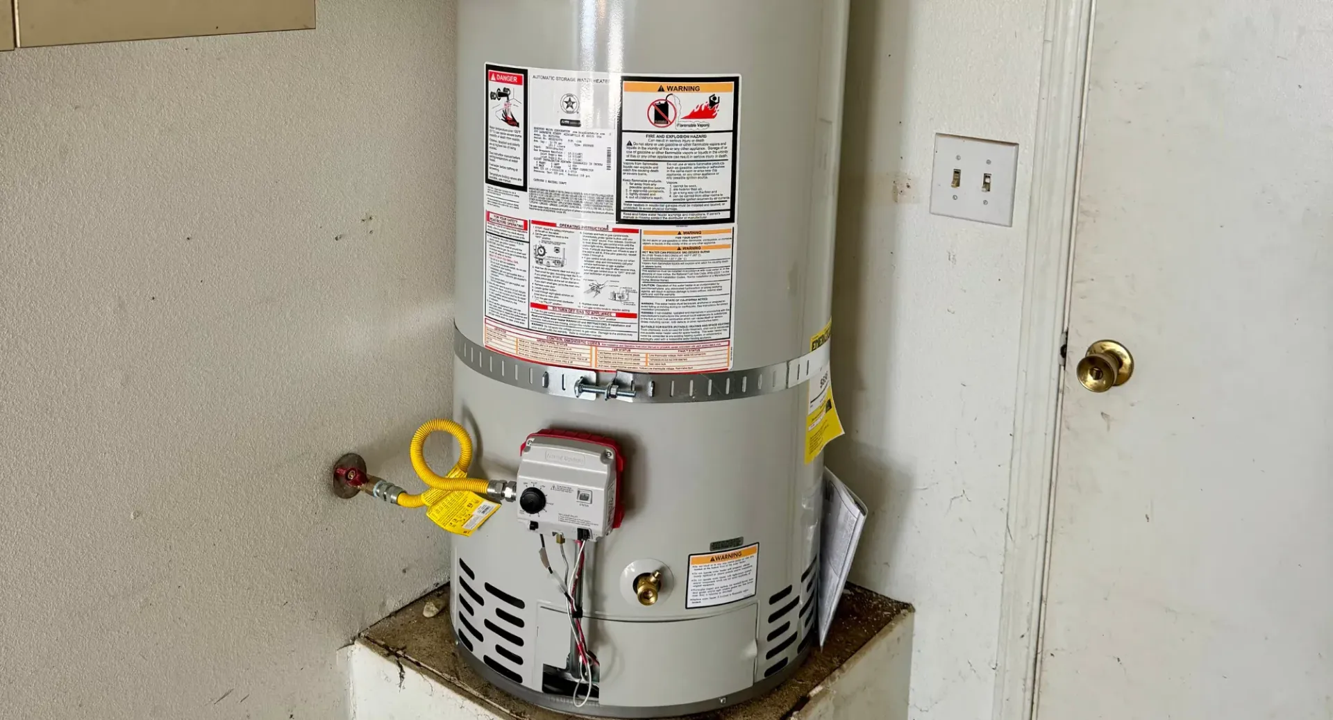 A water heater is sitting on top of a shelf next to a door.