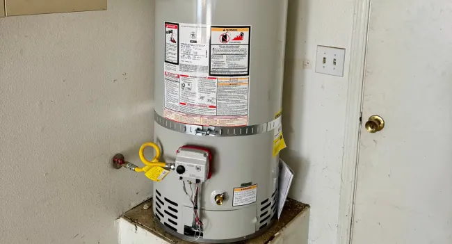 A water heater is sitting on top of a shelf next to a door.