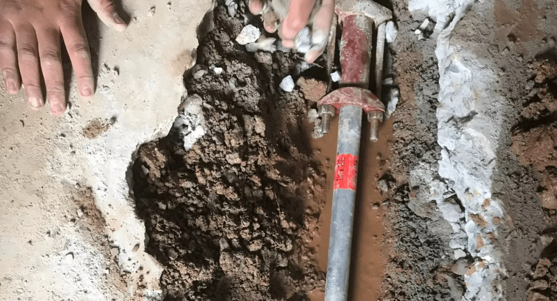 A person is holding a metal pipe in a hole in the ground.